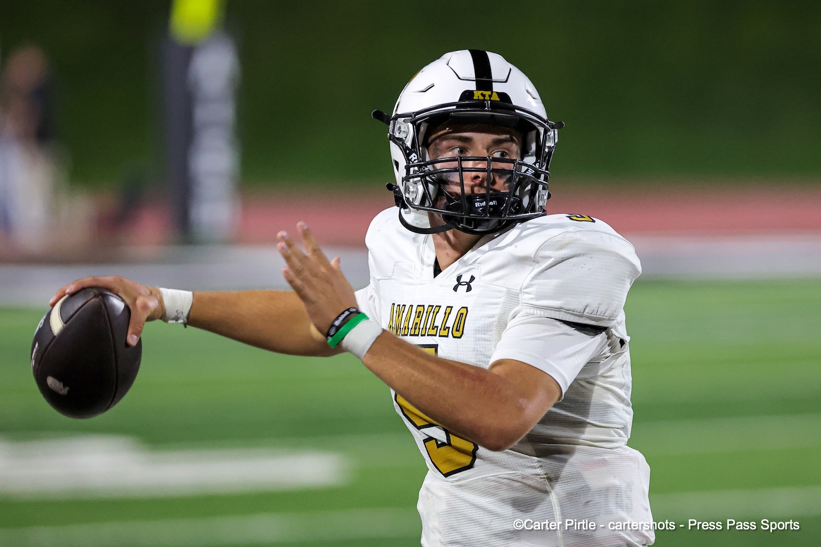 Quarterback in white uniform throws a football during a game, focused on the throw with green field in background.