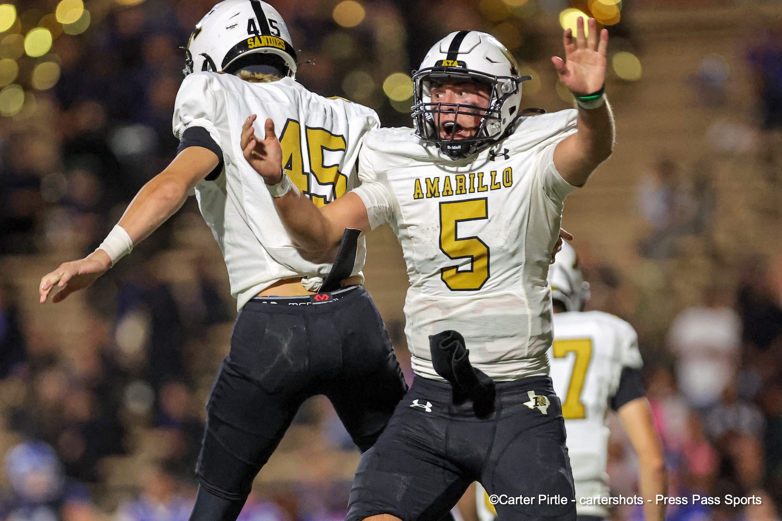 Amarillo football players celebrate a play, jumping and high-fiving on the field at night.