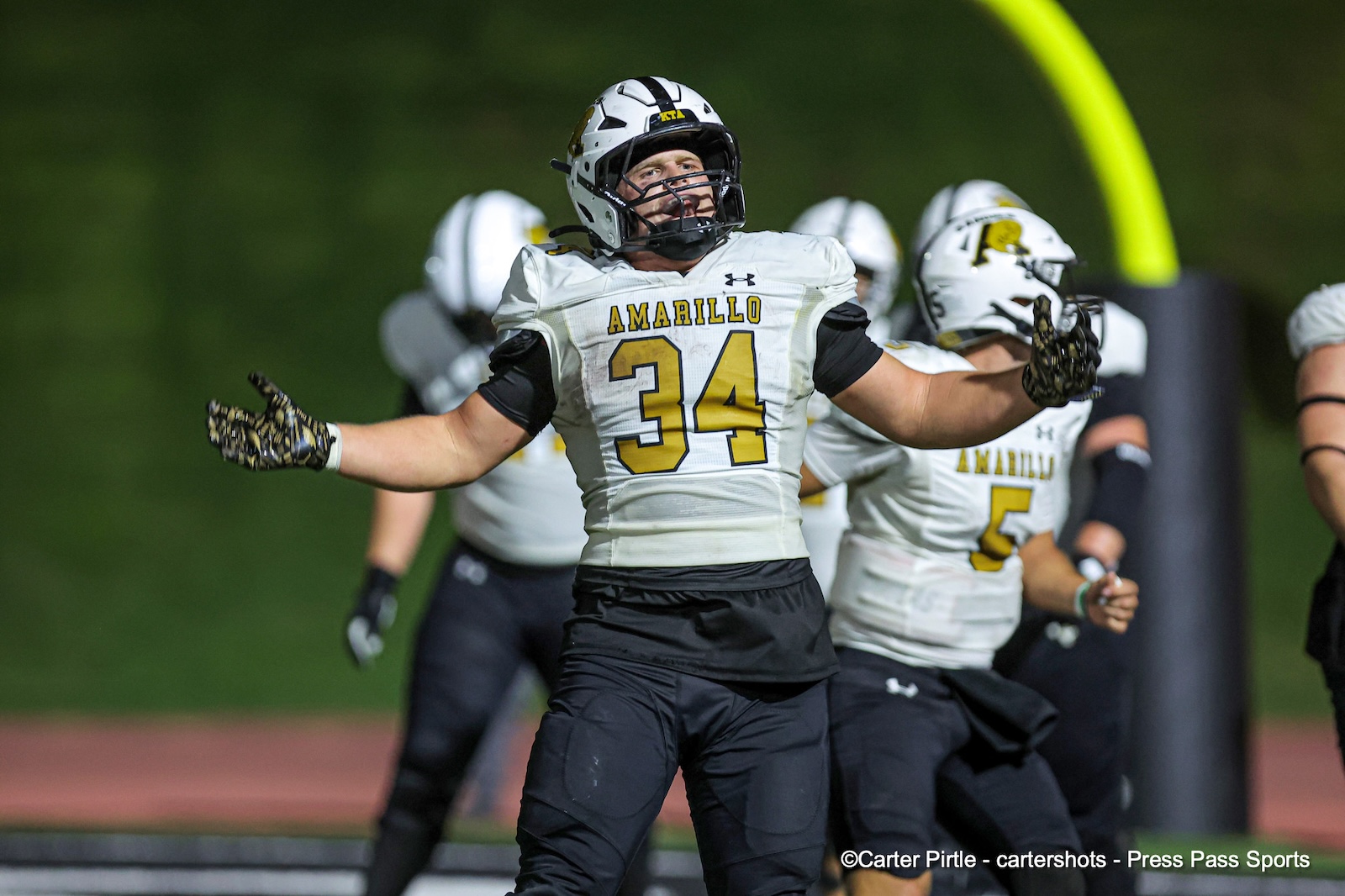 American football player in white Amarillo jersey #34 holds arms wide on the field, celebrating with teammates in the background.