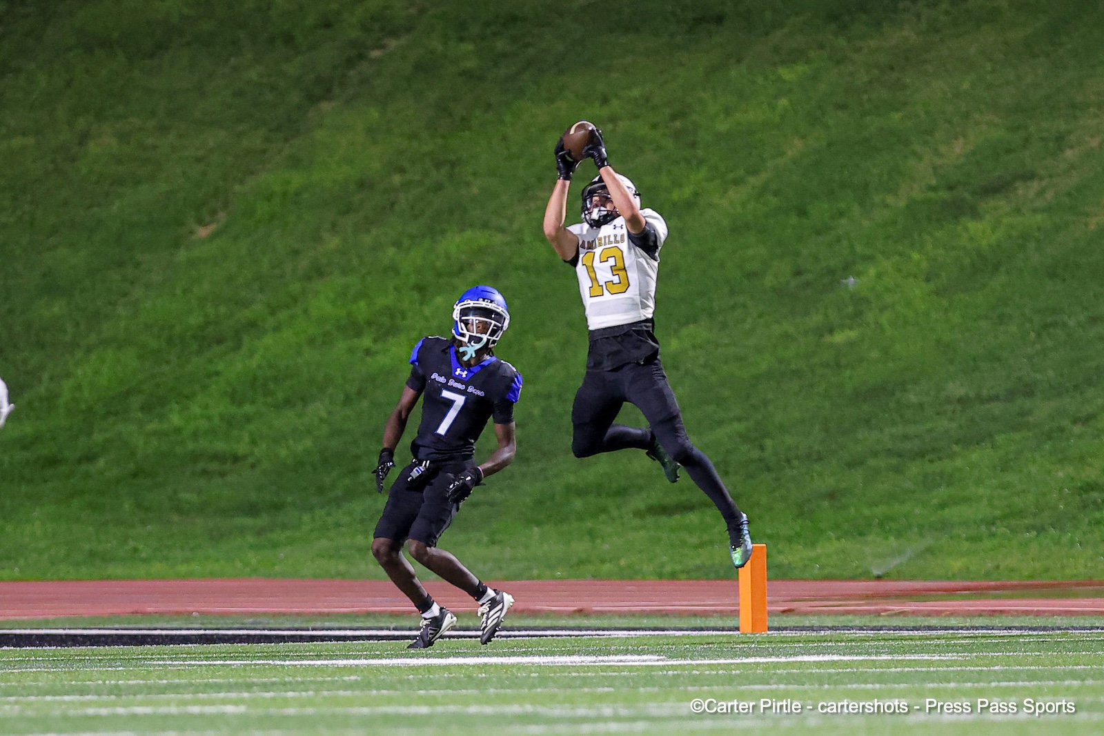 Football player in white jersey number 13 leaps to catch a pass near the orange end-zone pylon as a defender in black watches from below.