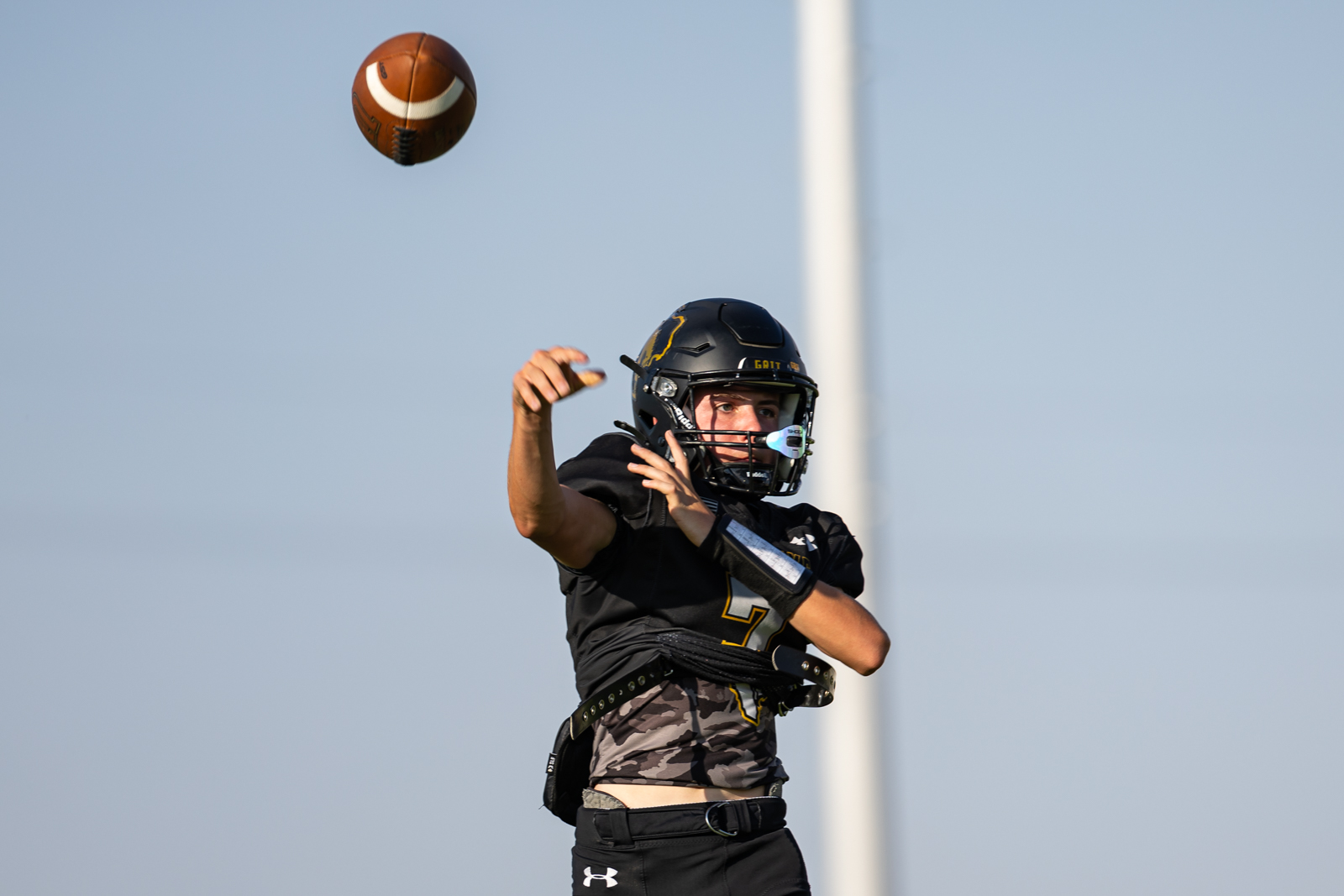 HHS-NHS-FB-1 | Press Pass Sports Quarterback in black uniform throwing a football mid‑air during a game, with helmet and protective gear visible.