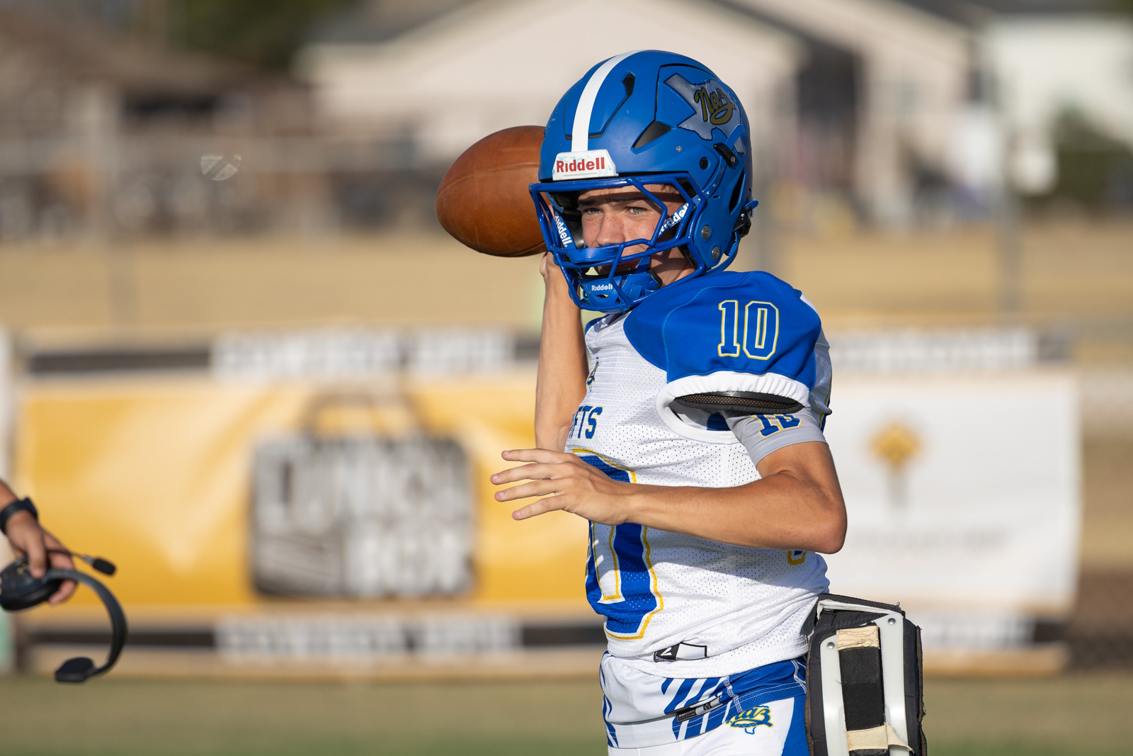 HHS-NHS-FB-4 | Press Pass Sports Football quarterback in blue and white uniform throws a pass on a sunny field, wearing a blue helmet with number 10.
