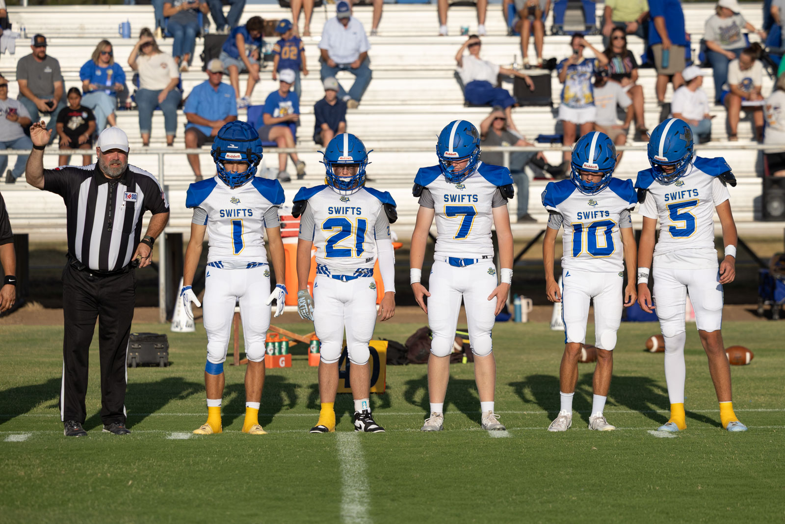HHS-NHS-FB-10 | Press Pass Sports Youth football team lined up on the field with referee raising a hand, players in blue and white uniforms marked'SWIFTS' and numbers 1, 2, 7, 10, 5, stands in background.