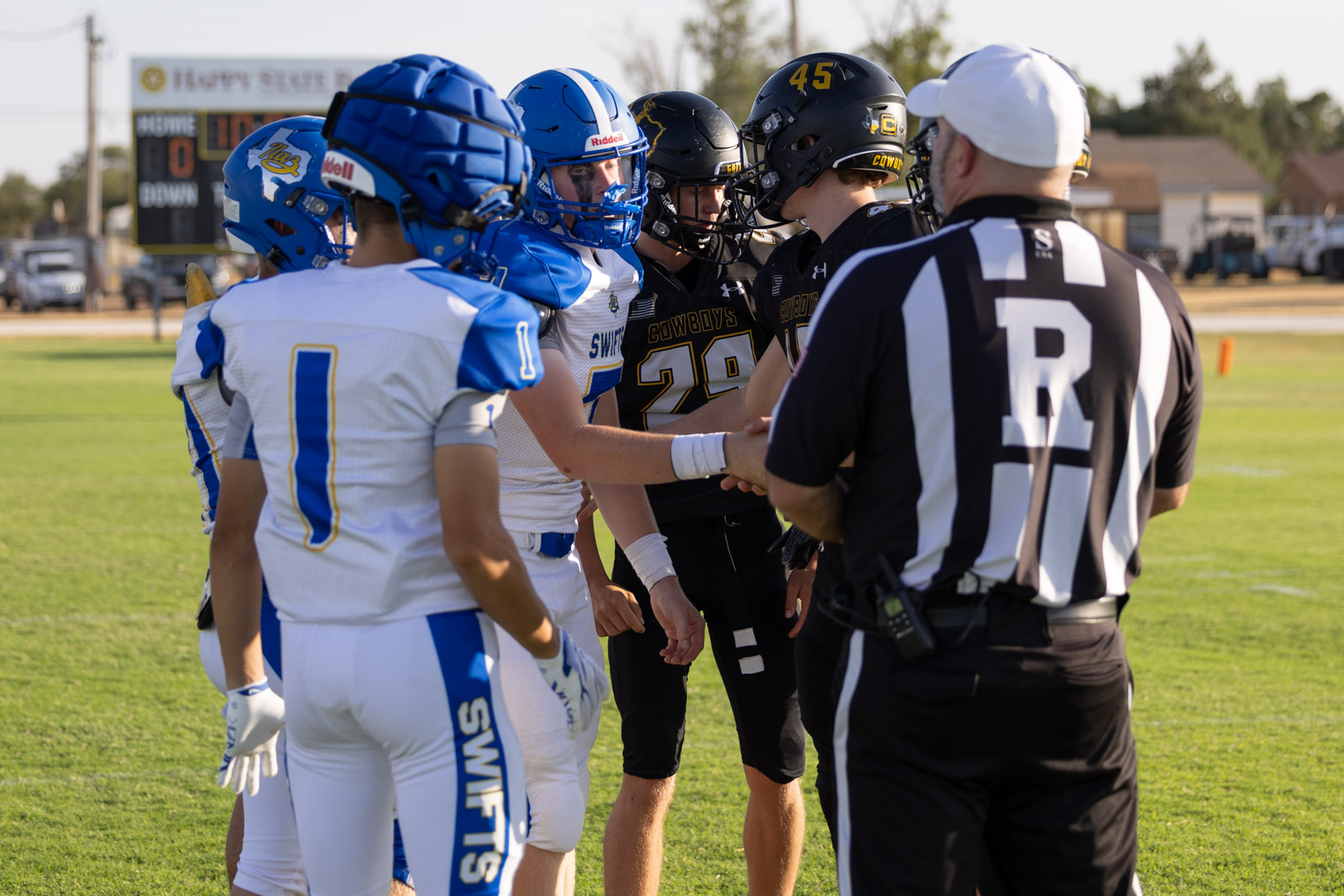 HHS-NHS-FB-11 | Press Pass Sports Football players from two teams shake hands before a game on a sunny field, with a referee in the foreground.