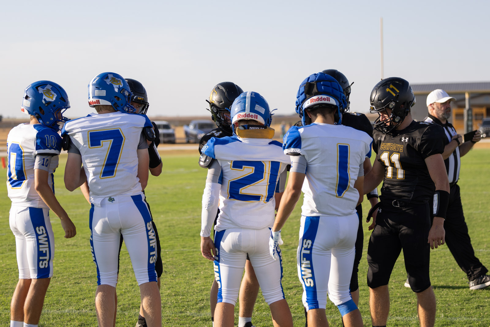 HHS-NHS-FB-13 | Press Pass Sports Group of football players in blue-and-white uniforms huddling on a green field before a game.