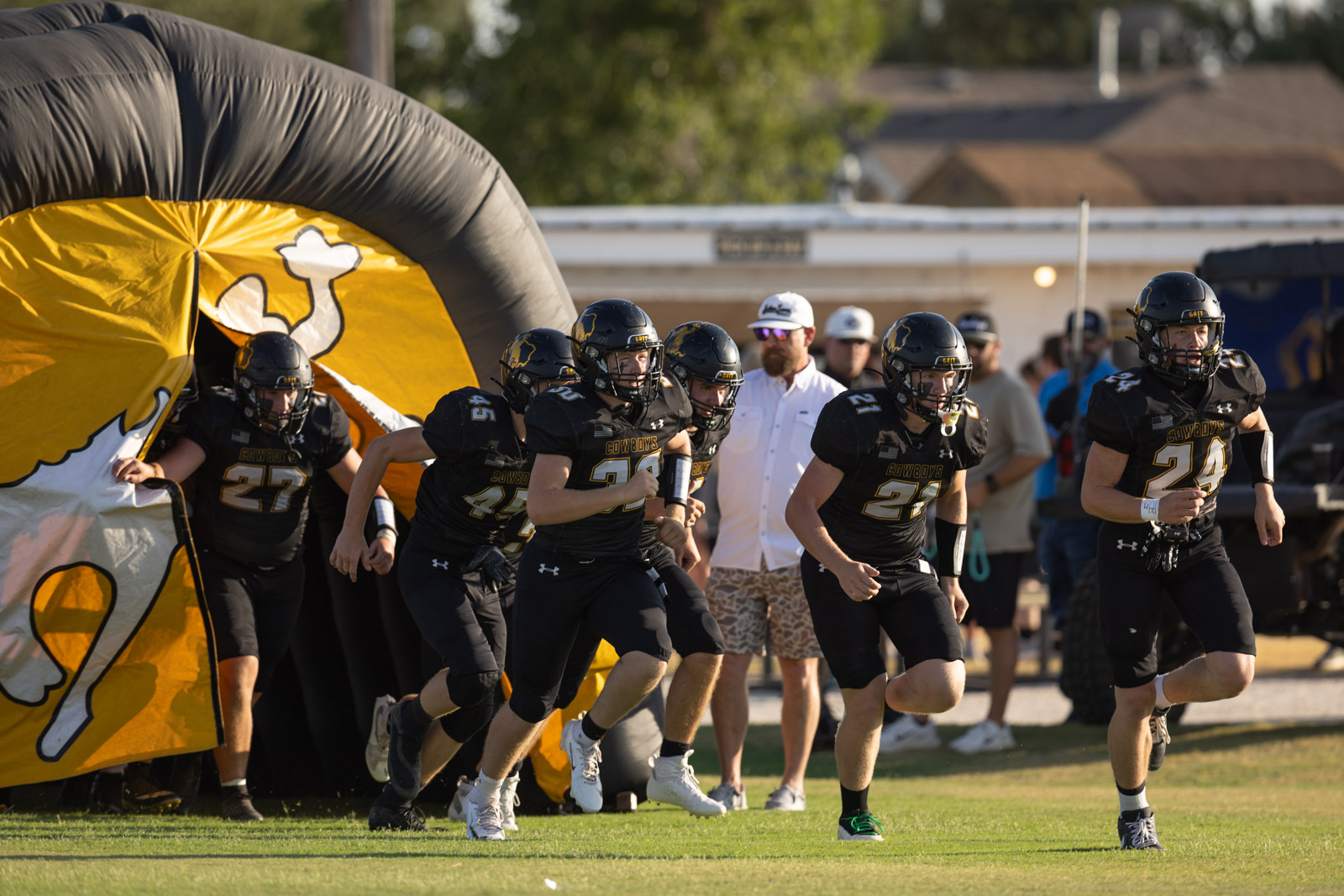 HHS-NHS-FB-14 | Press Pass Sports Football players in black uniforms sprint onto the field from a large yellow tunnel inflatable.
