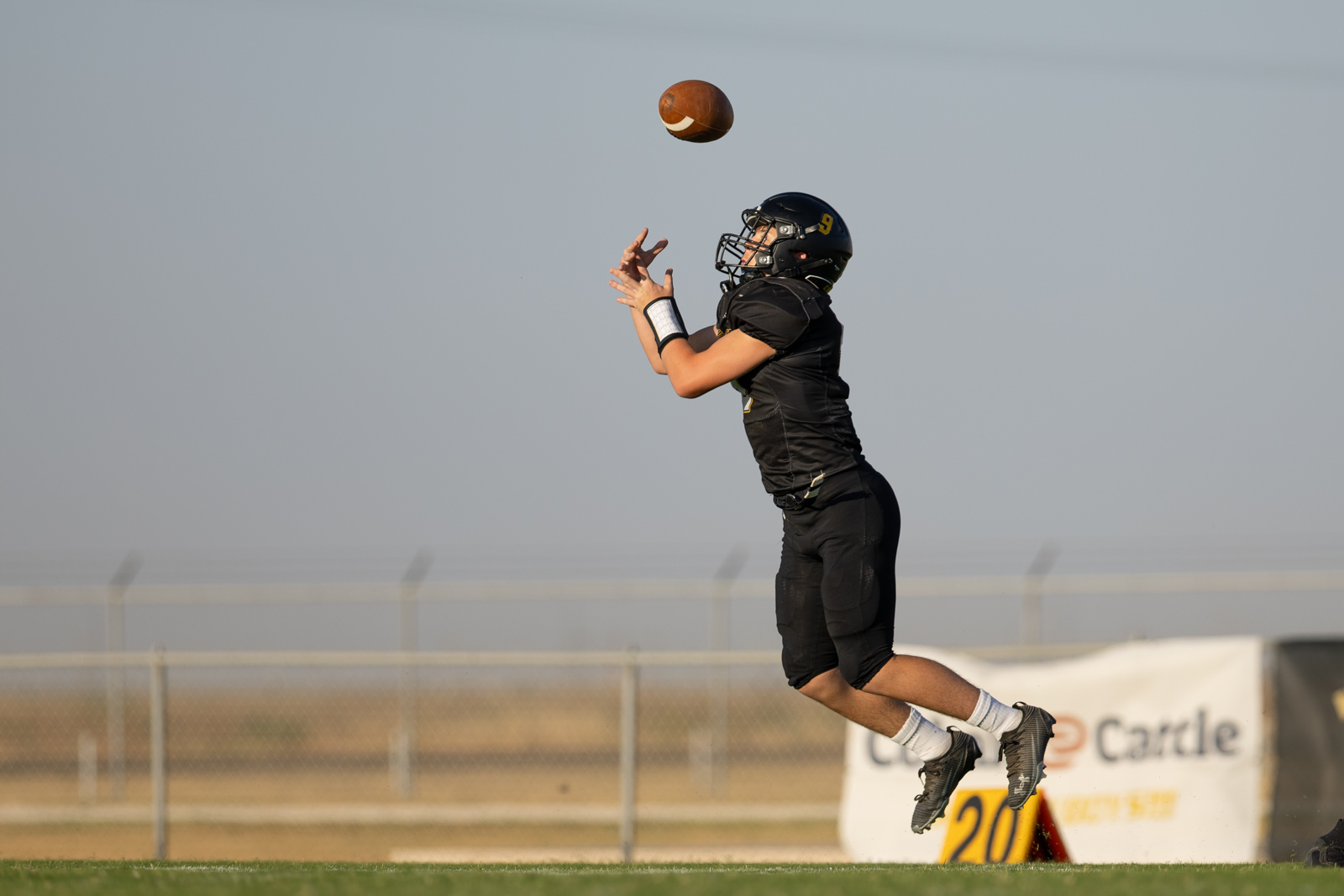 HHS-NHS-FB-16 | Press Pass Sports Football player in a black uniform leaps to catch a pass on an outdoor field.