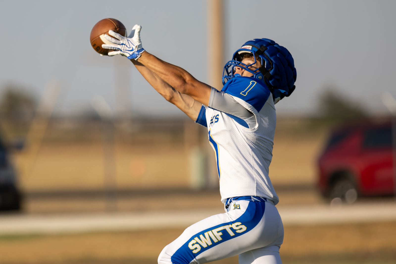 HHS-NHS-FB-18 | Press Pass Sports Football player in white and blue uniform leaping to catch a pass in mid-air, wearing a blue helmet and gloves