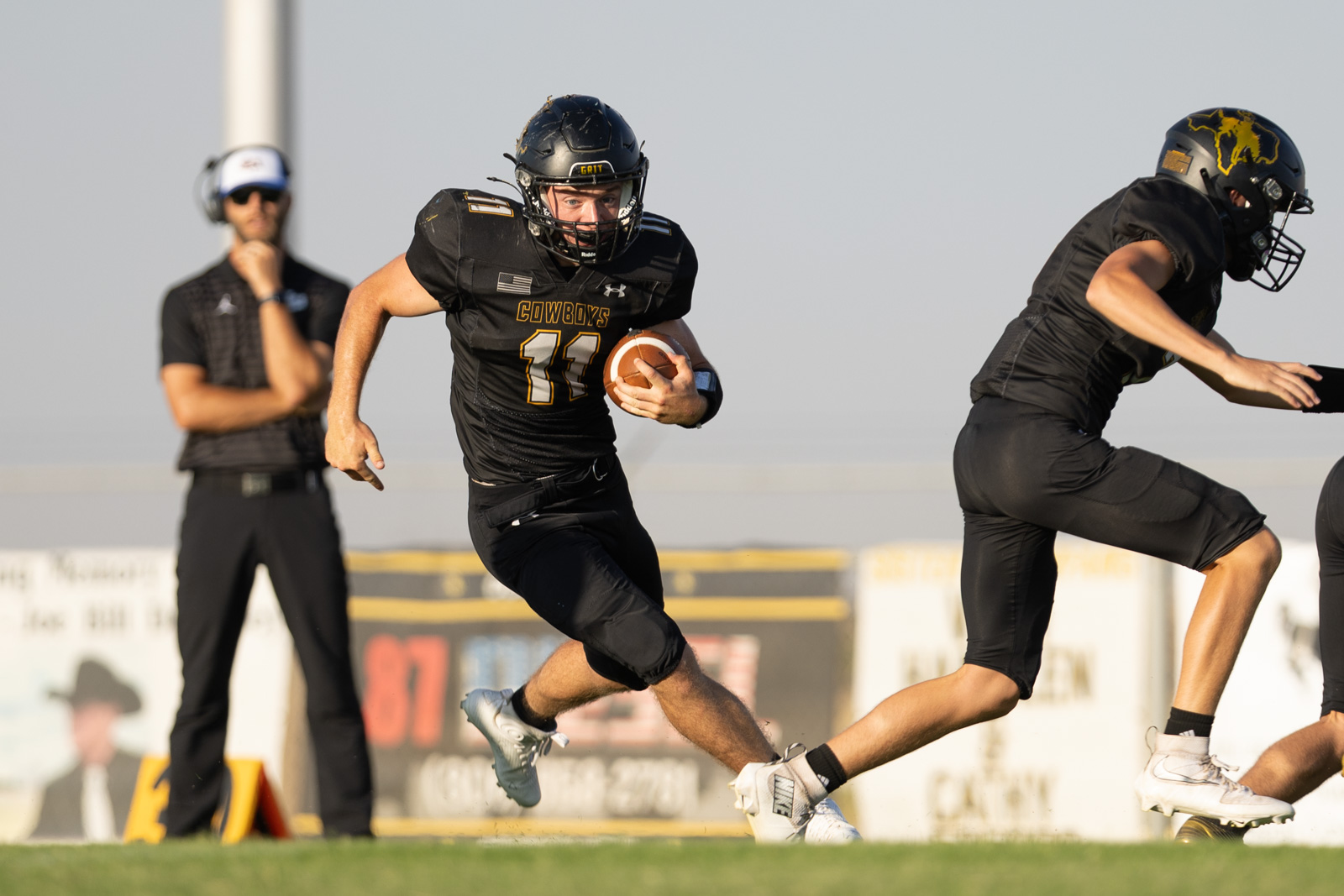 HHS-NHS-FB-21 | Press Pass Sports Cowboys running back (number 11) sprints with the ball as a defender closes in, coach in background watching.