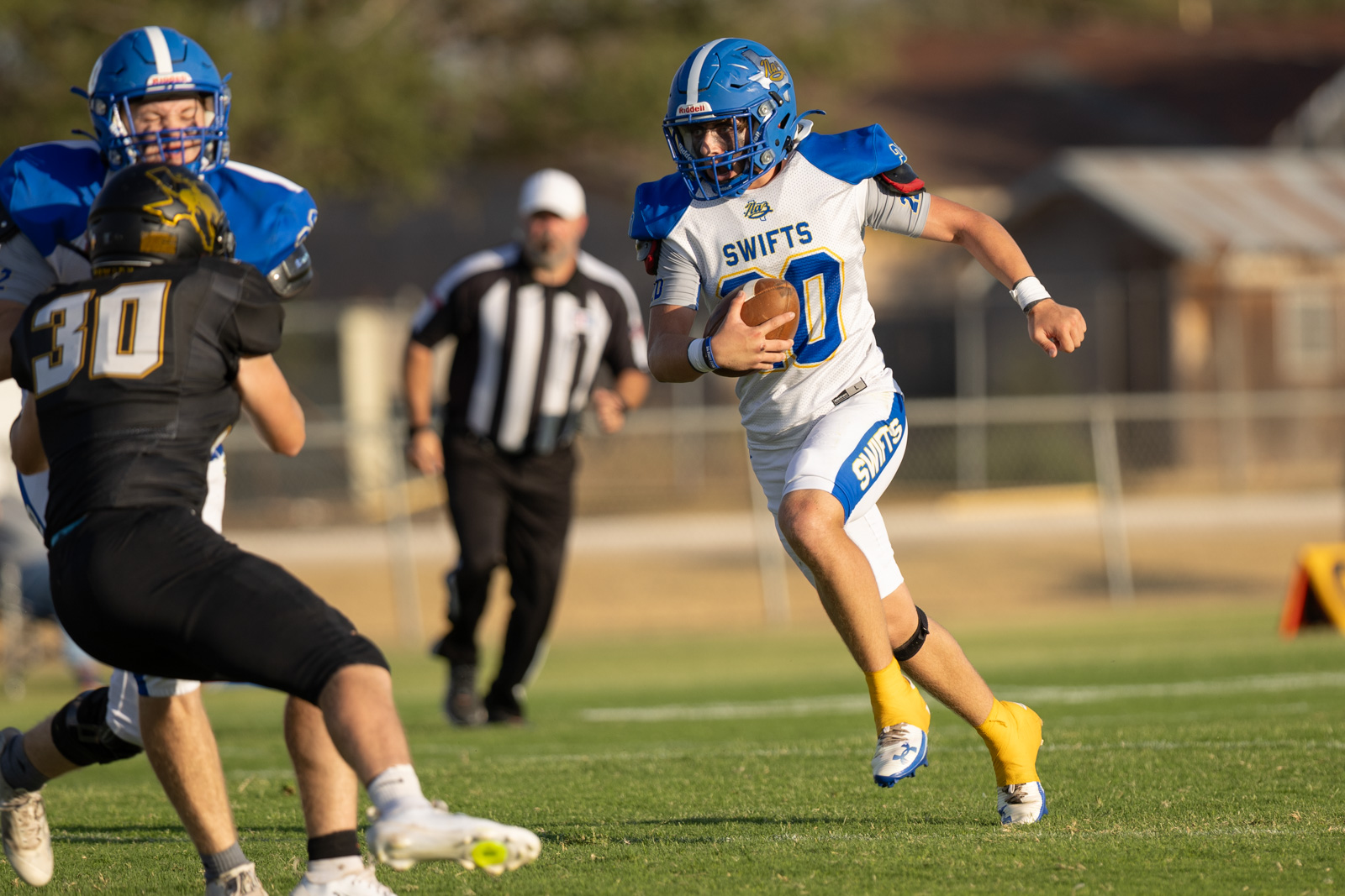 HHS-NHS-FB-23 | Press Pass Sports Football player in white/blue Swift uniform runs with the ball during a game, chased by opponents on a sunny field.