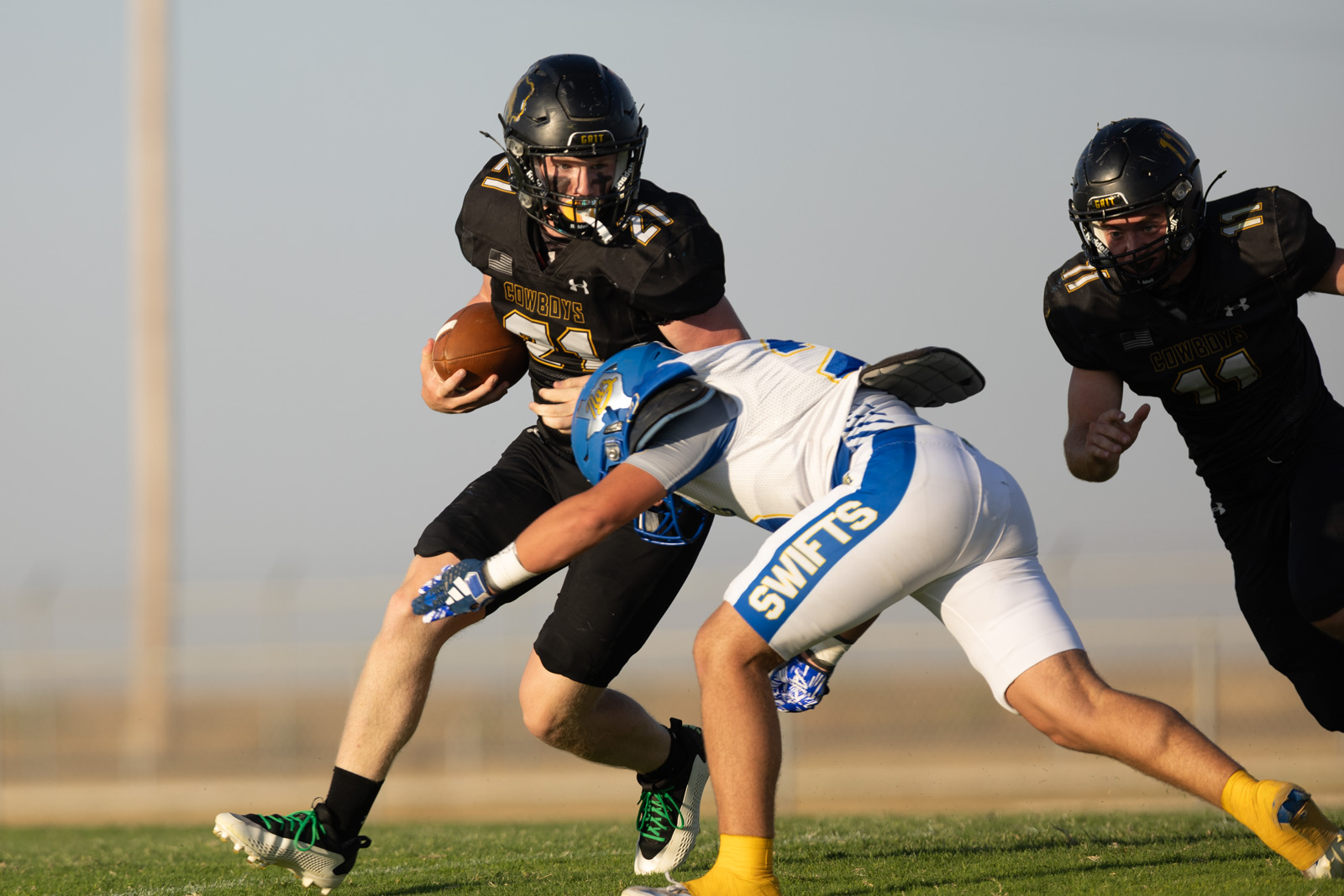 HHS-NHS-FB-28 | Press Pass Sports Cowboys player in black jersey runs with the football as a Swift defender in white and blue reaches in.