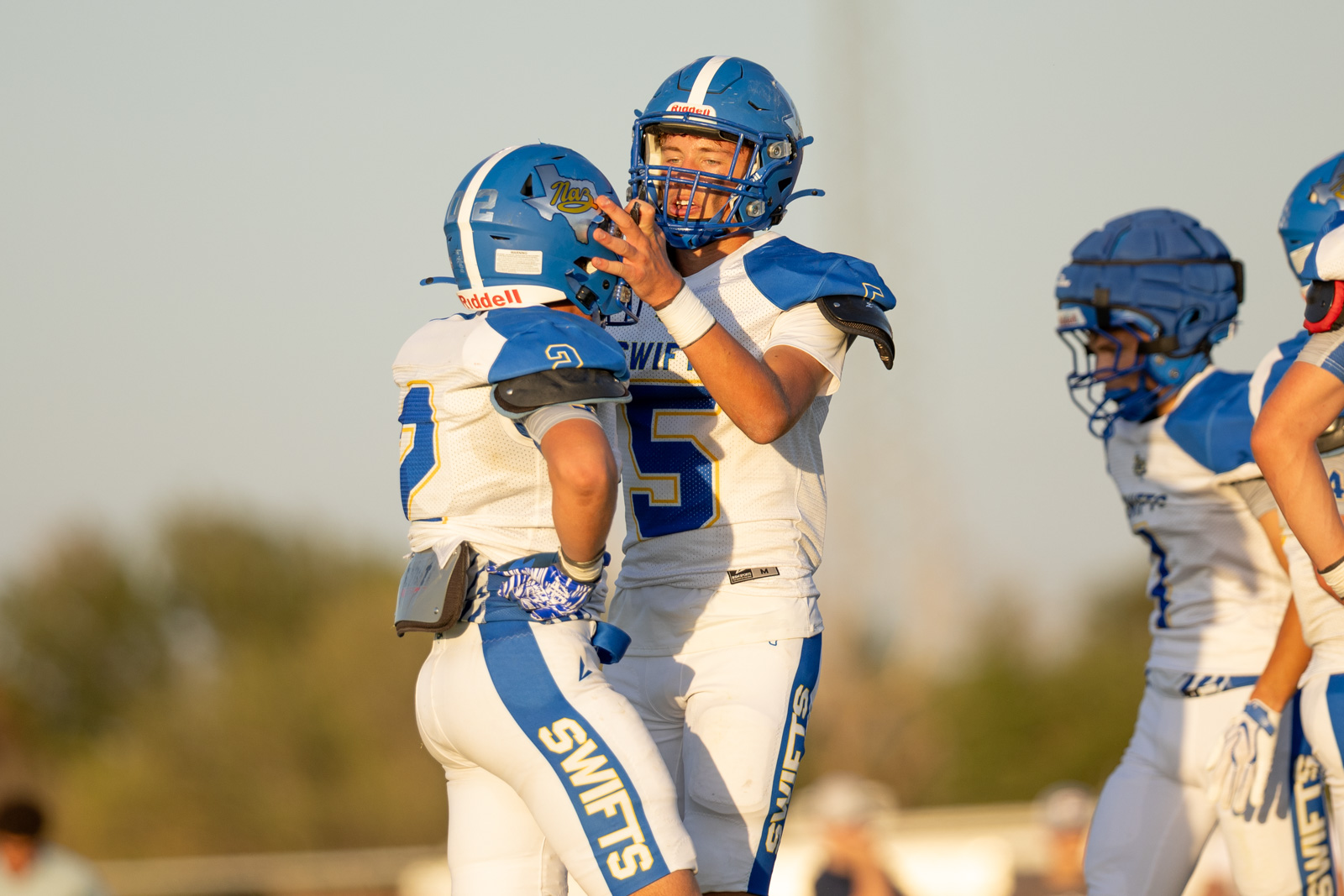 HHS-NHS-FB-42 | Press Pass Sports Two football players in blue and white celebrate, embracing on the field during a game moment.