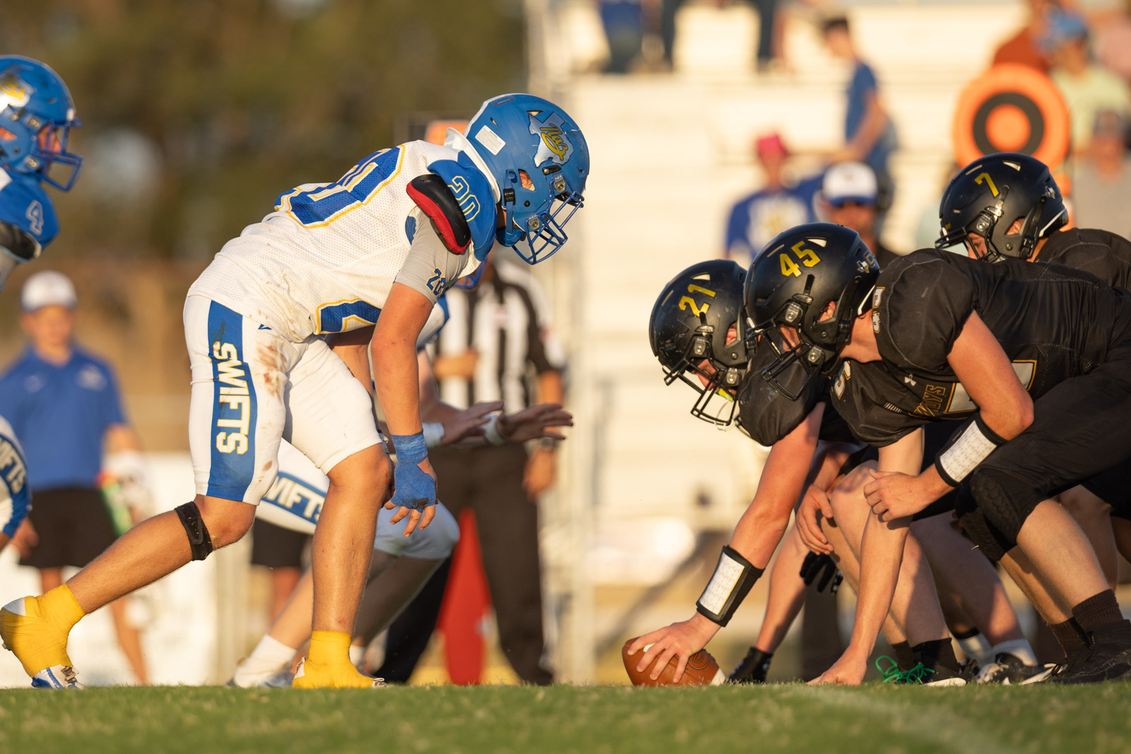 HHS-NHS-FB-43 | Press Pass Sports High school football players line up at the line of scrimmage, white-and-blue vs black uniforms, preparing to snap the ball to start play.