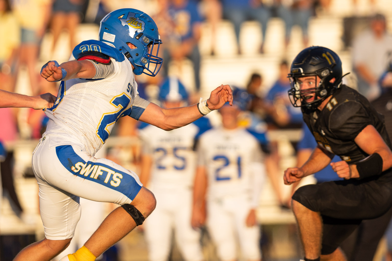 HHS-NHS-FB-44 | Press Pass Sports Football players in action: a white-and-blue team player (#20) lunging toward an opposing black-uniform defender as a tackle ensues.