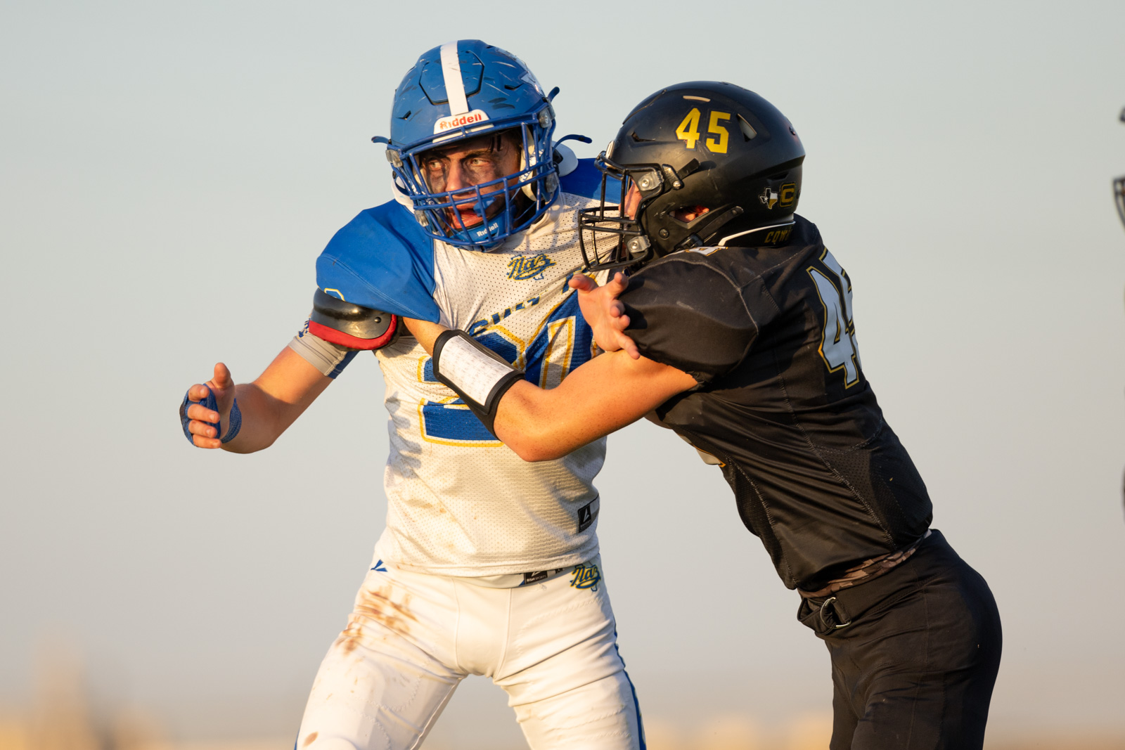 HHS-NHS-FB-46 | Press Pass Sports Two football players collide during a game: one in a blue helmet and white/blue uniform, the other in black with number 45.