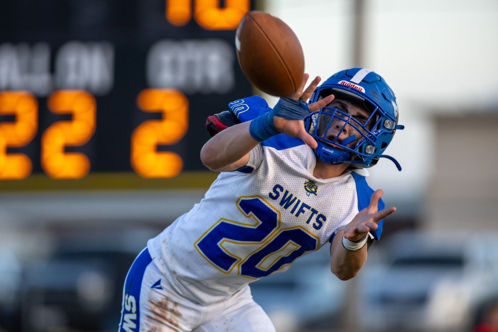 HHS-NHS-FB-51 | Press Pass Sports Football player in blue and white reaching to catch a pass, blue helmet, #28 Swifts, ball just above his hands.