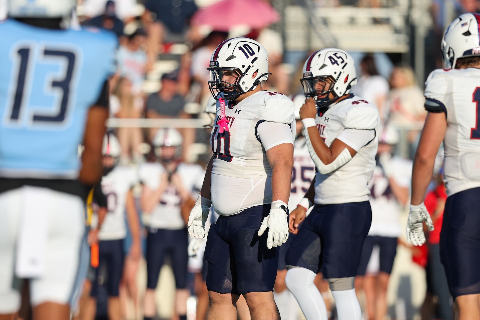 Seabolt Chase-14136 | Press Pass Sports Football players in white uniforms and helmets standing on a sideline during a game, number 10 and 45 visible, crowd in background
