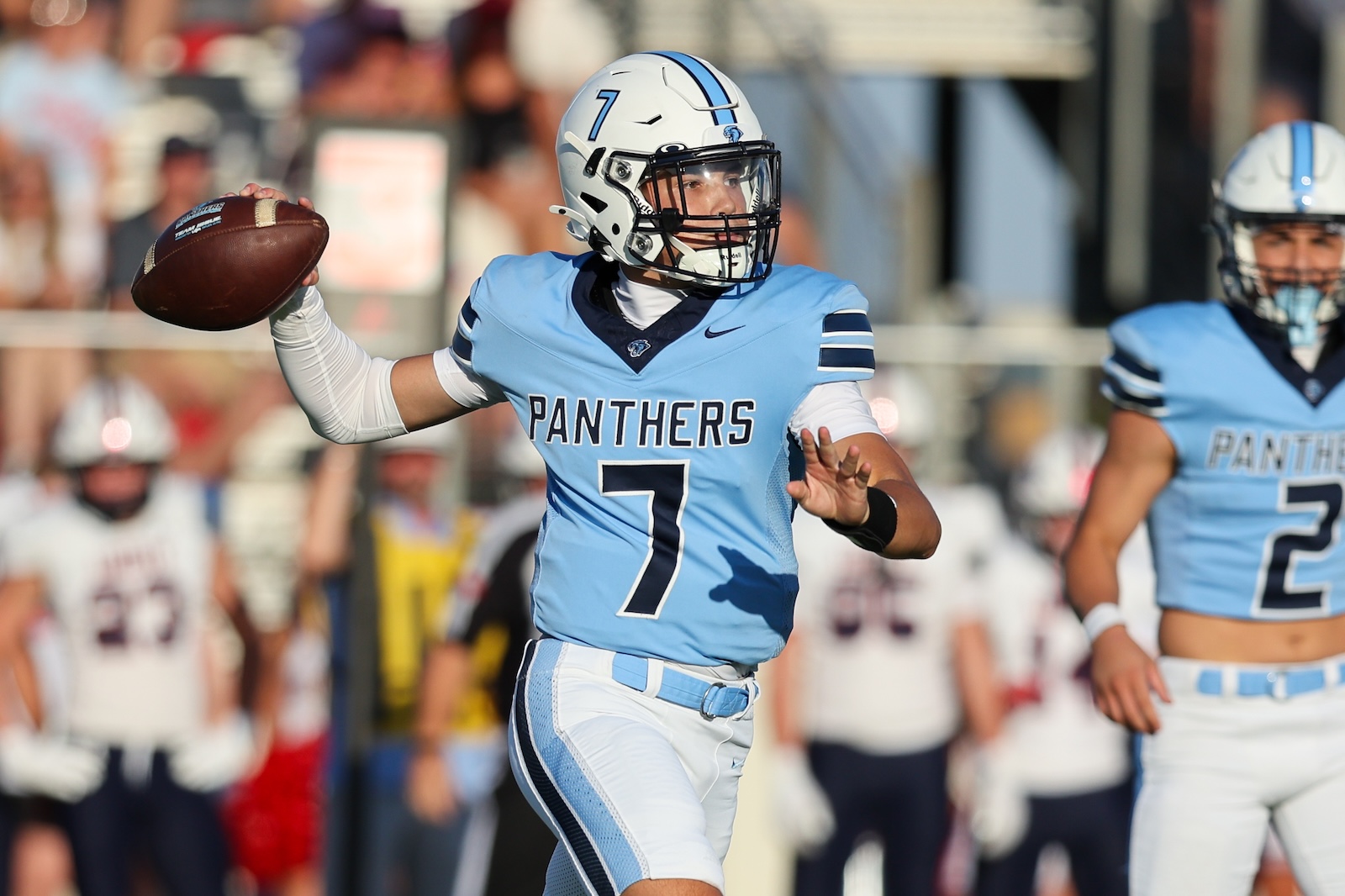 Seabolt Chase-14180 | Press Pass Sports Panthers quarterback wearing number 7 in a light-blue uniform throws a pass during a game with a crowd in the background, and a teammate nearby.