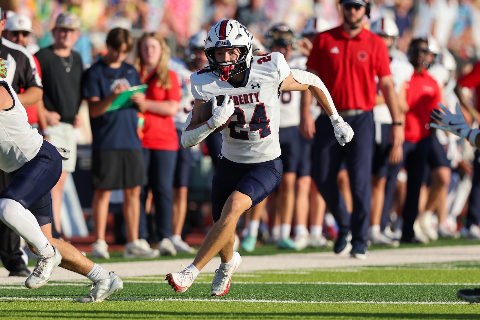 Seabolt Chase-14210 | Press Pass Sports Football player wearing a white Liberty jersey #24 runs with the ball during a game, crowded sideline in the background.