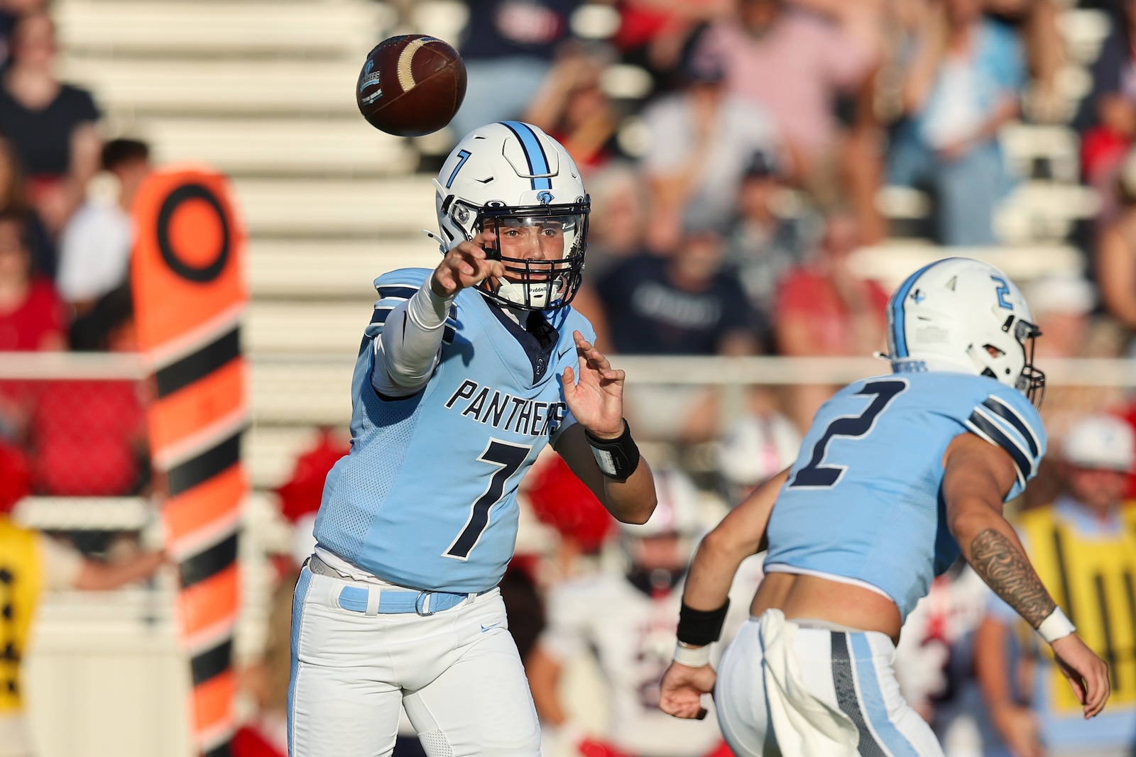 Seabolt Chase-14273 | Press Pass Sports Quarterback in light blue Panthers uniform releasing a pass during a game, with teammates and a crowd in the background.