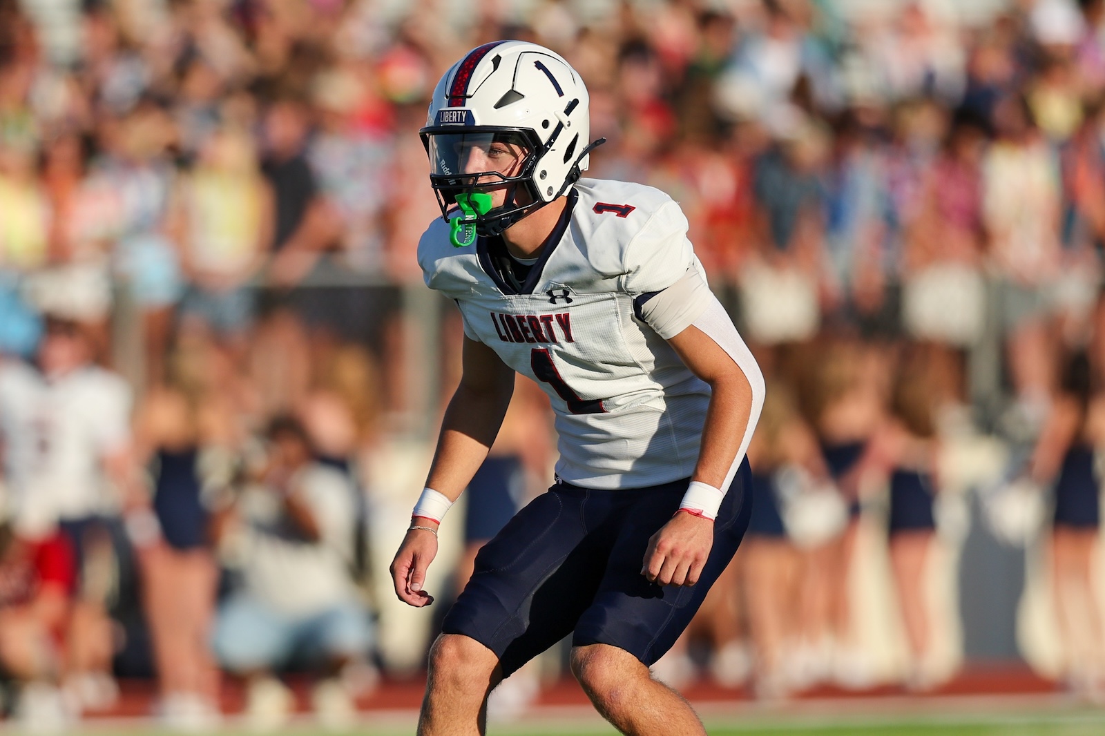 Seabolt Chase-14299 | Press Pass Sports American football player in a white Liberty jersey numbered 1 on a sunny field with a cheering crowd in the background.