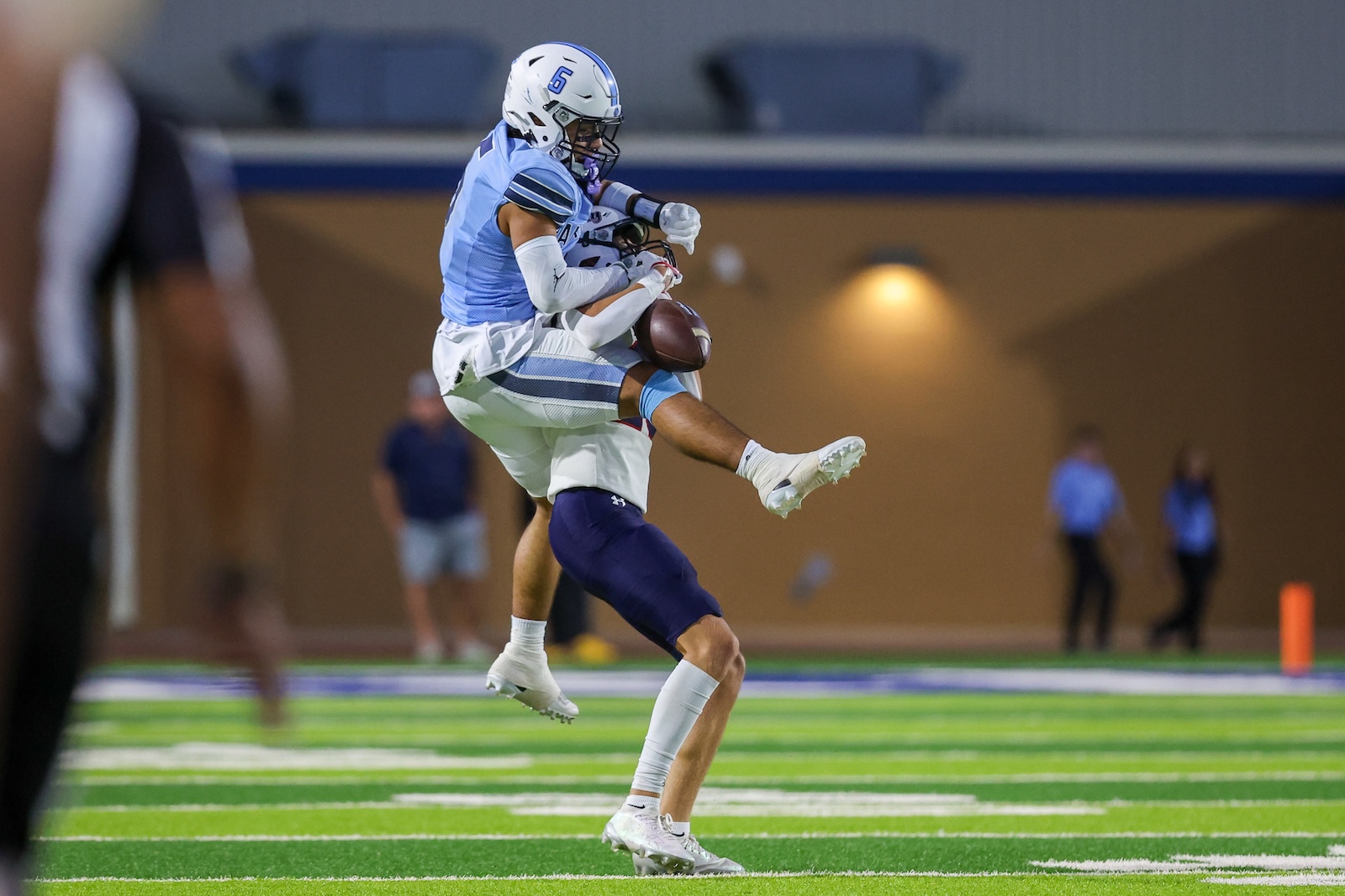 Seabolt Chase-15521 | Press Pass Sports Two football players in blue and white jerseys contest a loose ball mid-air on a brightly lit indoor field.