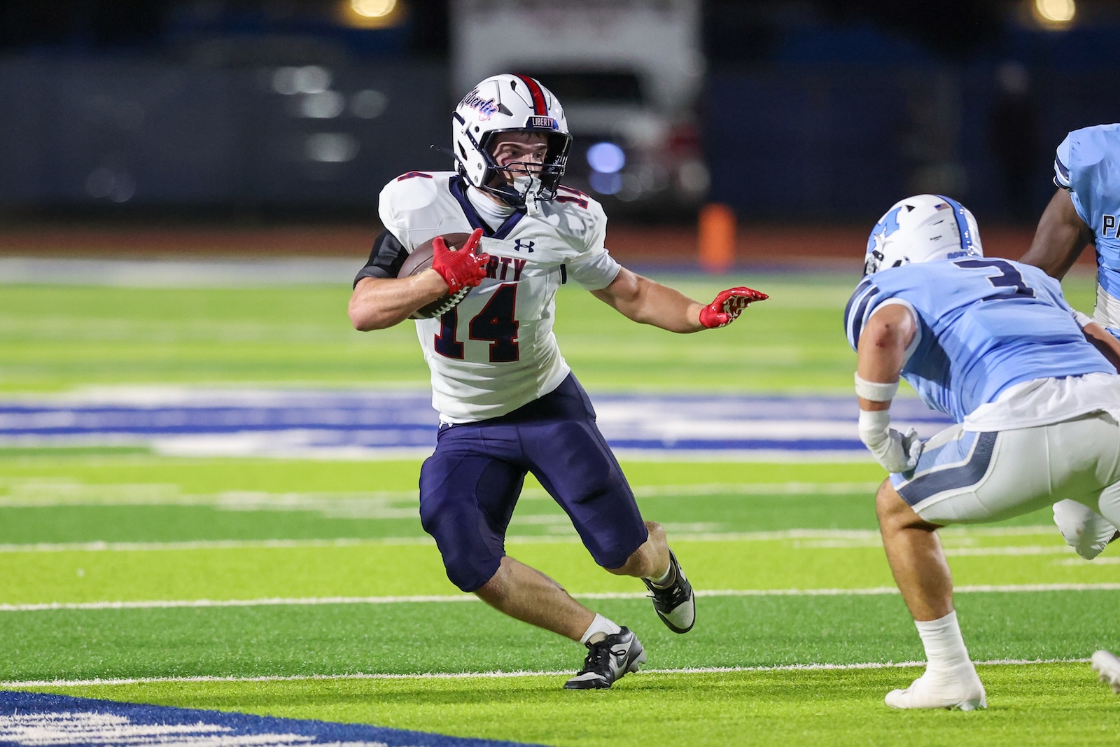 Seabolt Chase-15934 | Press Pass Sports Football player wearing white jersey #14 dashes with the ball while a defender closes in on a lit turf field at night.