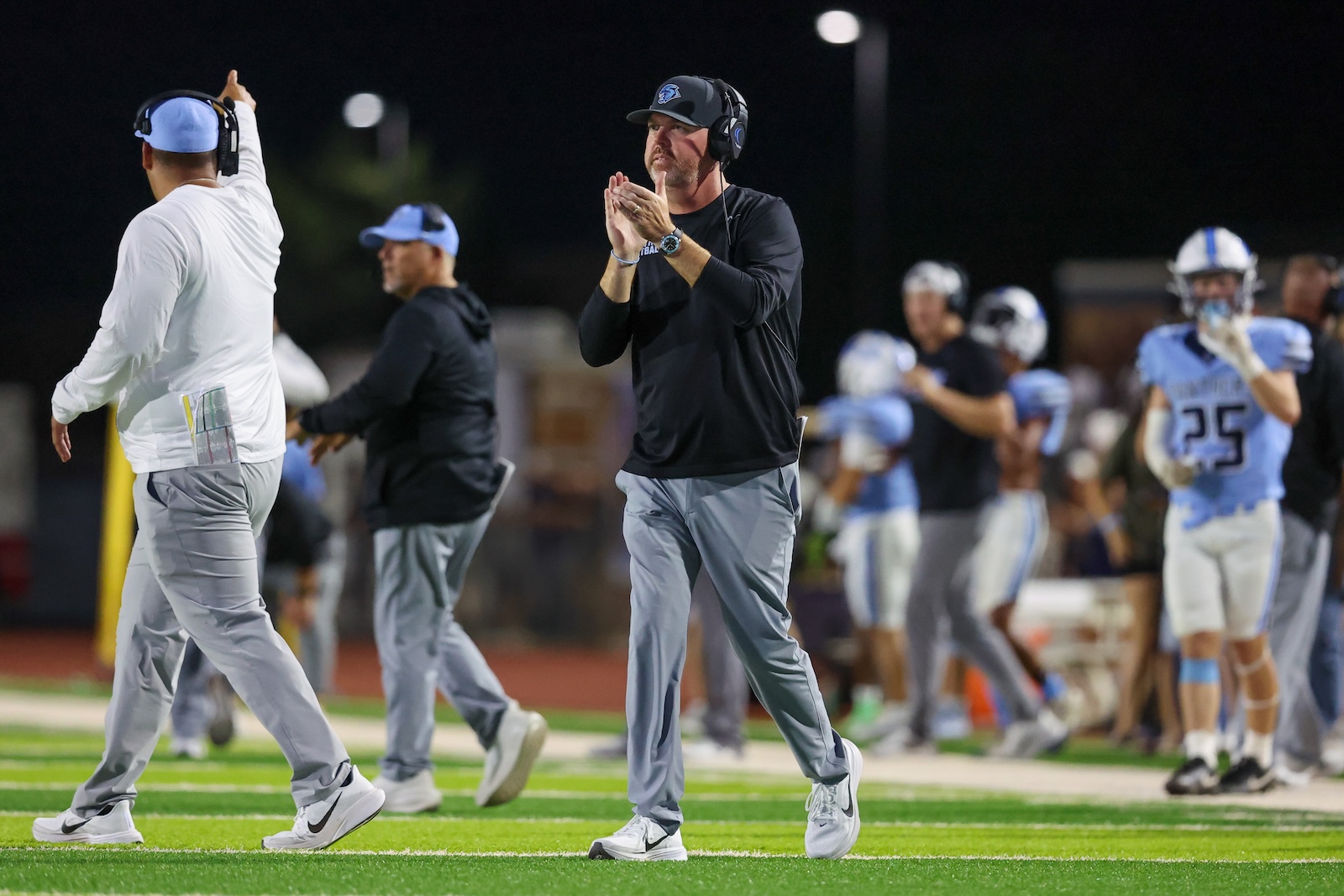 Seabolt Chase-16265 | Press Pass Sports Football coaches and players walk on a night field, with a coach in black shirt clapping as teammates pass by.