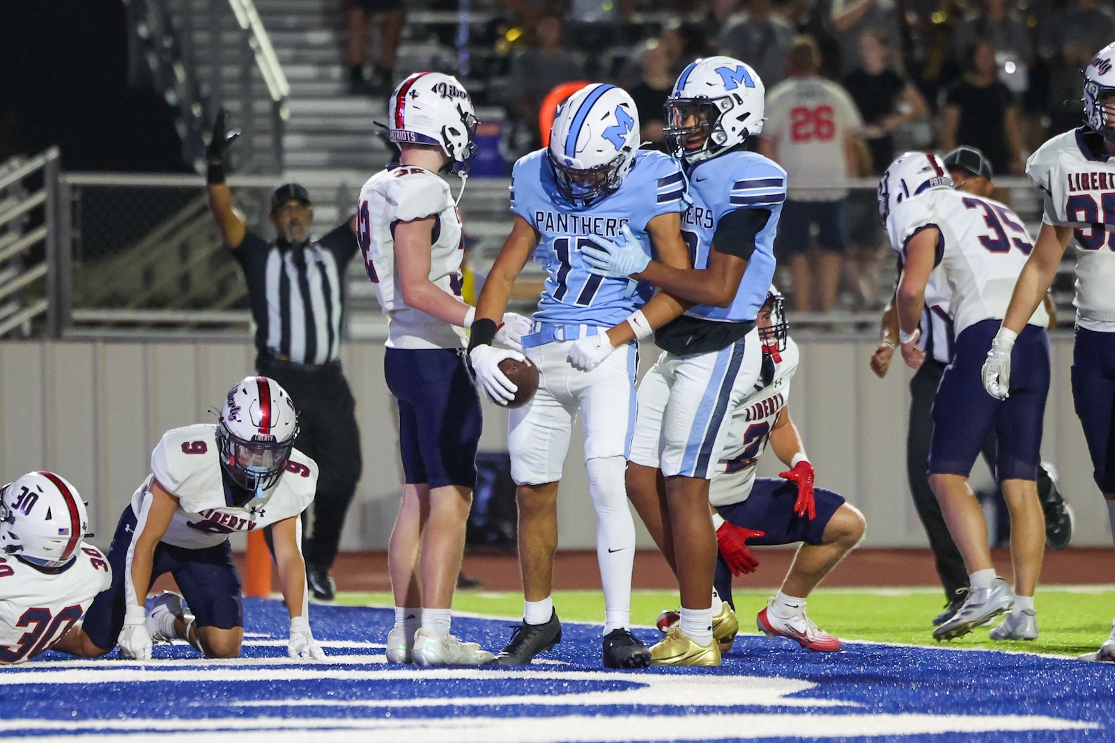 Seabolt Chase-25073 | Press Pass Sports Panthers player in blue jersey (#11) holds a football while a teammate in blue supports him in the end zone, surrounded by opponents in white uniforms.