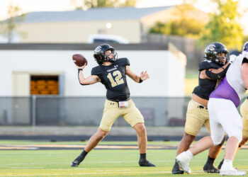 panhnandle-vs-canadian-football-jpegJoe-pps-9 | Press Pass Sports Quarterback in a black jersey (number 12) throws a football during a high school game while teammates block nearby on a green turf field.