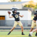 panhnandle-vs-canadian-football-jpegJoe-pps-9 | Press Pass Sports Quarterback in a black jersey (number 12) throws a football during a high school game while teammates block nearby on a green turf field.