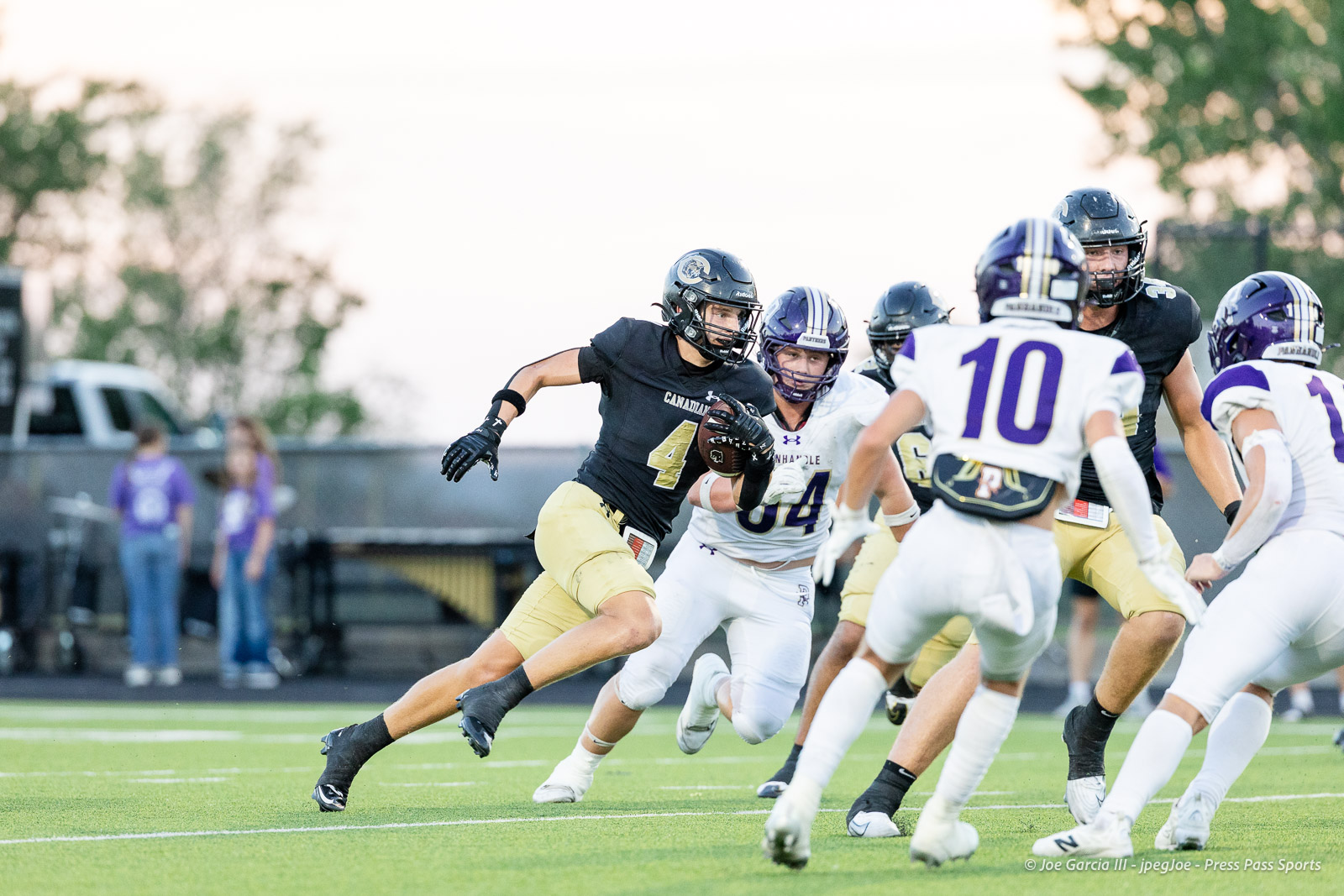 panhnandle-vs-canadian-football-jpegJoe-pps-17 | Press Pass Sports Football player in black jersey with number 4 runs with ball while defenders in white pursue on a green field.