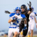 HHS-NHS-FB-52 | Press Pass Sports Football player in blue-and-white jersey runs with the ball while an opponent in black reaches from behind, on a sideline field.