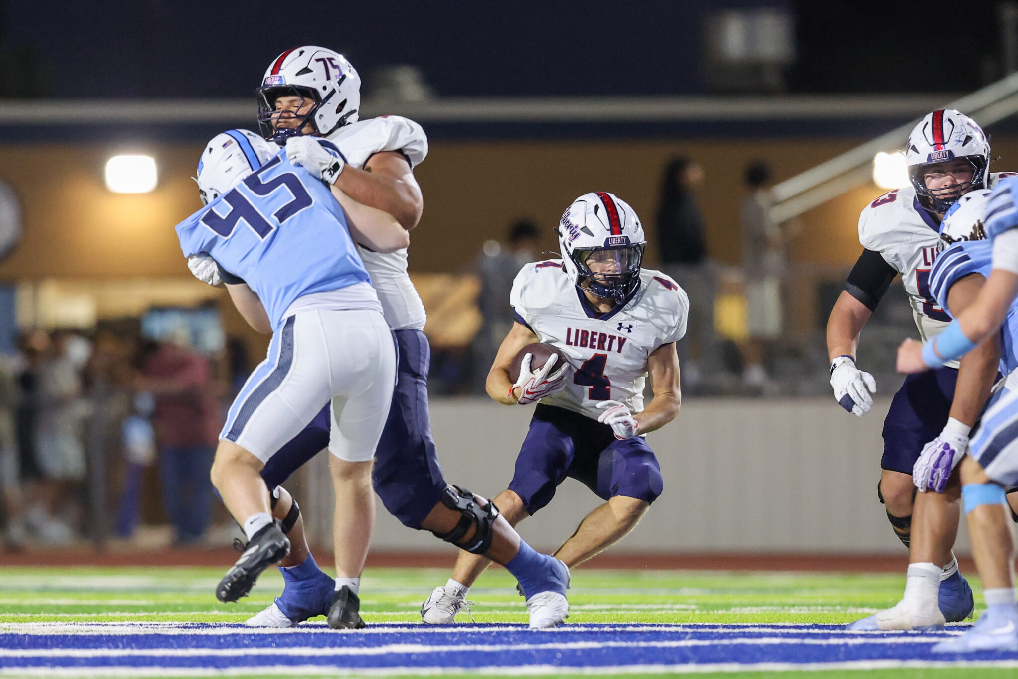 Seabolt Chase-15874 | Press Pass Sports Football game action: a Liberty player in white jersey runs with the ball while a blue-team defender grabs him from behind under stadium lights.