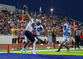 Seabolt Chase-24733 | Press Pass Sports Player in white jersey reaches for a football over the goal line as teammates cheer in a blue end zone while a crowded stands watches at night.