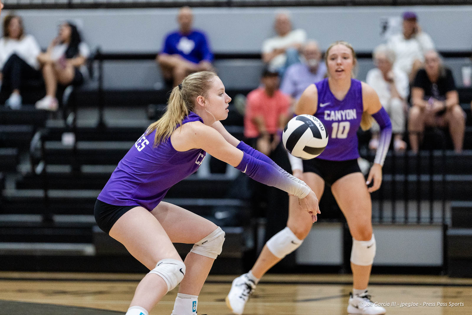 randall-showcase-2026-jpegJoe-pps-1 | Press Pass Sports Two female volleyball players in purple uniforms dive and reach to pass a ball during a rally in an indoor gymnasium.