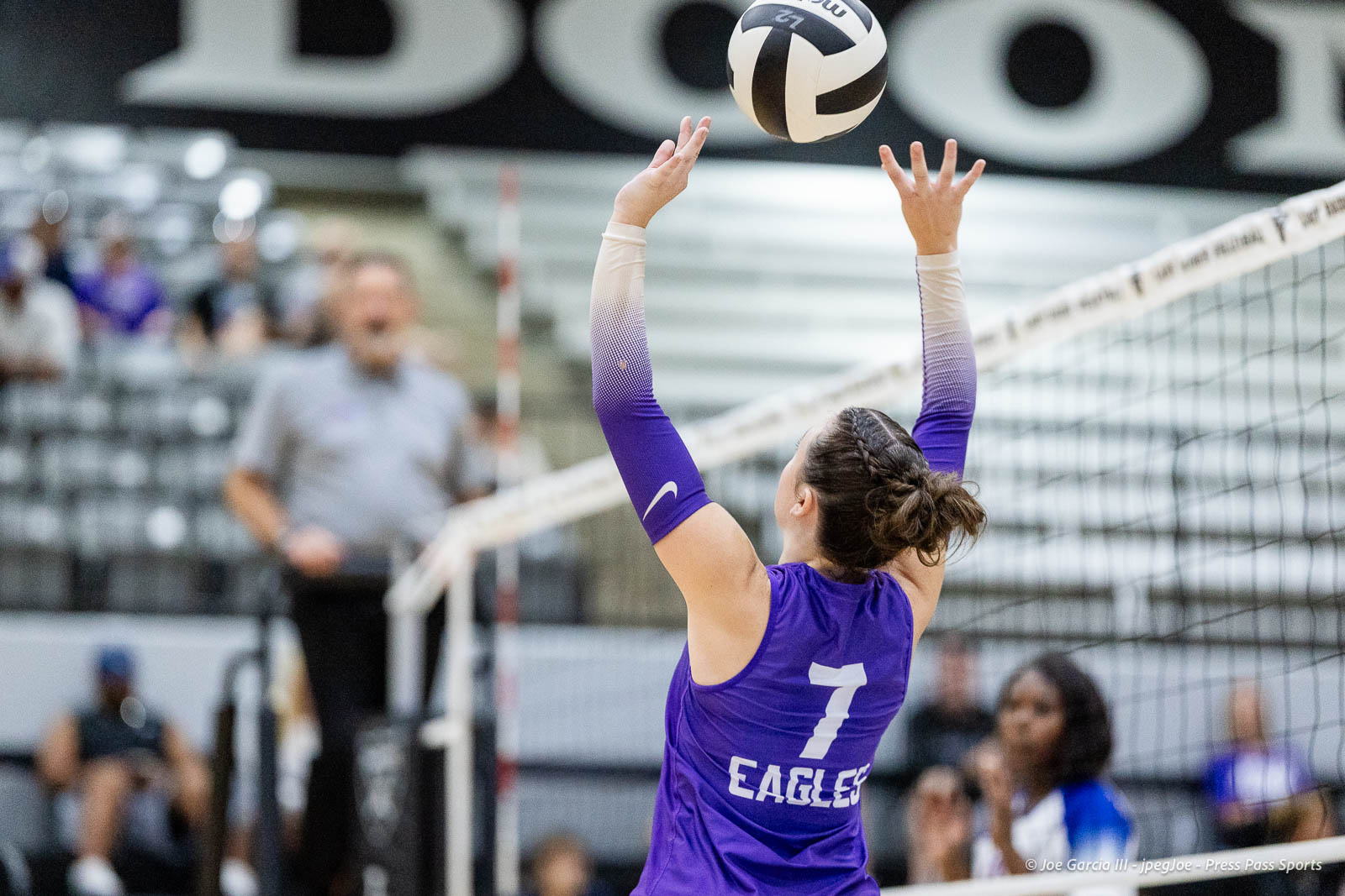 randall-showcase-2026-jpegJoe-pps-2 | Press Pass Sports Female volleyball player in a purple jersey (#7) raises hands to touch a ball at the net during an indoor match, with spectators in the blurred background.