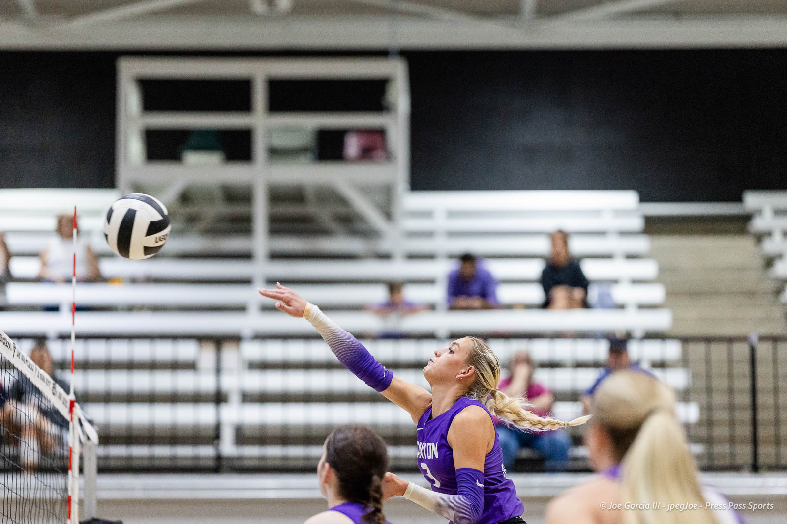 randall-showcase-2026-jpegJoe-pps-8 | Press Pass Sports Female volleyball player in a purple jersey reaching to hit the ball near the net during an indoor match, with spectators in bleachers in the background.