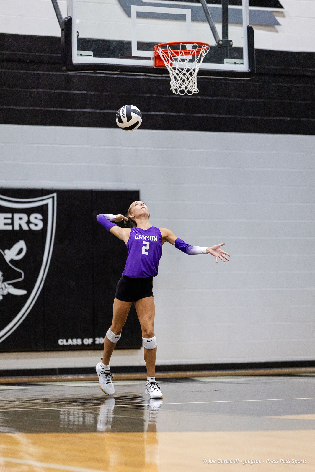 randall-showcase-2026-jpegJoe-pps-14 | Press Pass Sports Female volleyball player in a purple jersey (No. 2) serves the ball in a gymnasium with a basketball hoop overhead.