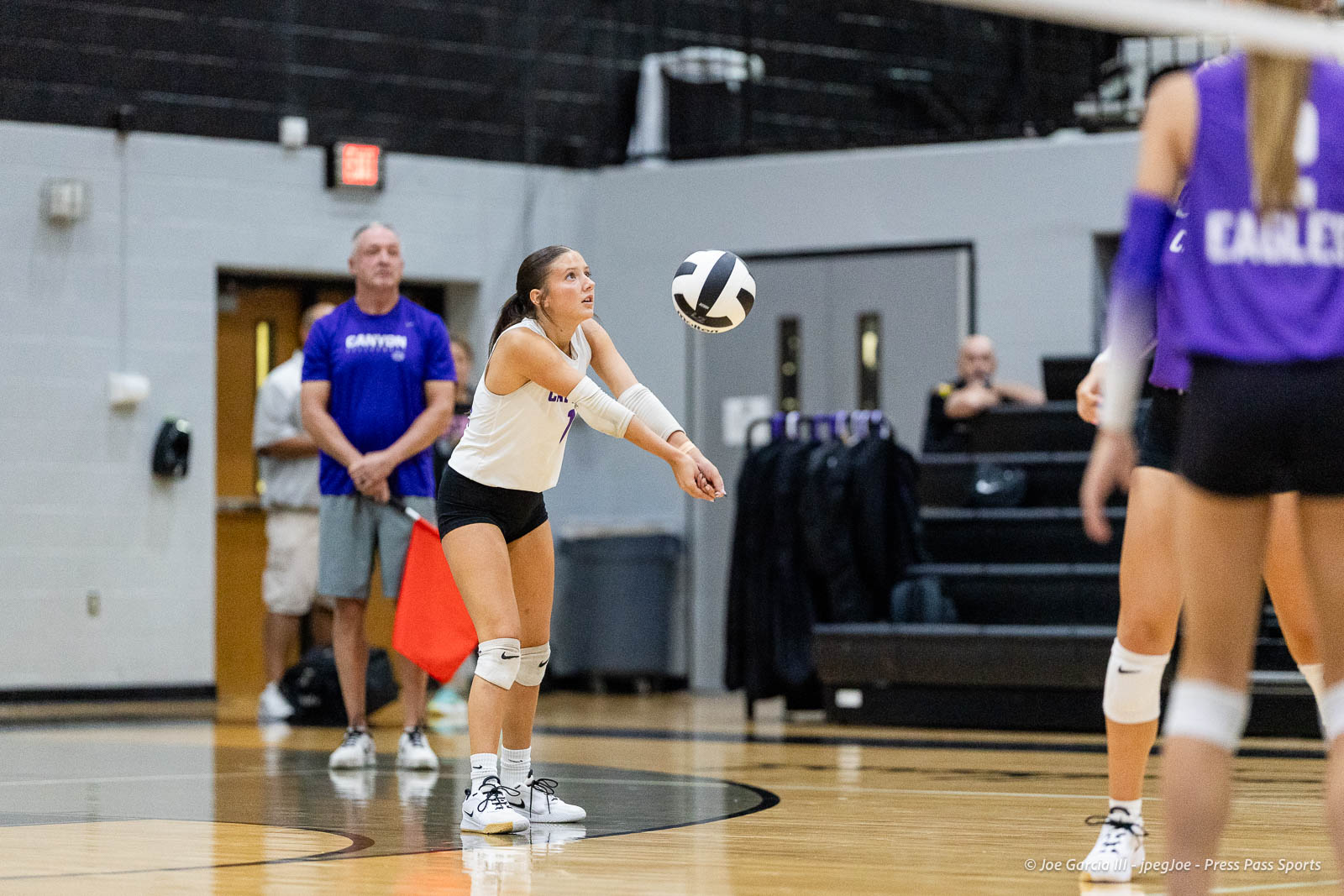 randall-showcase-2026-jpegJoe-pps-19 | Press Pass Sports Female volleyball player in a white jersey and knee pads uses a forearm pass to receive the ball in a gym, with teammates and a coach in blue in the background.