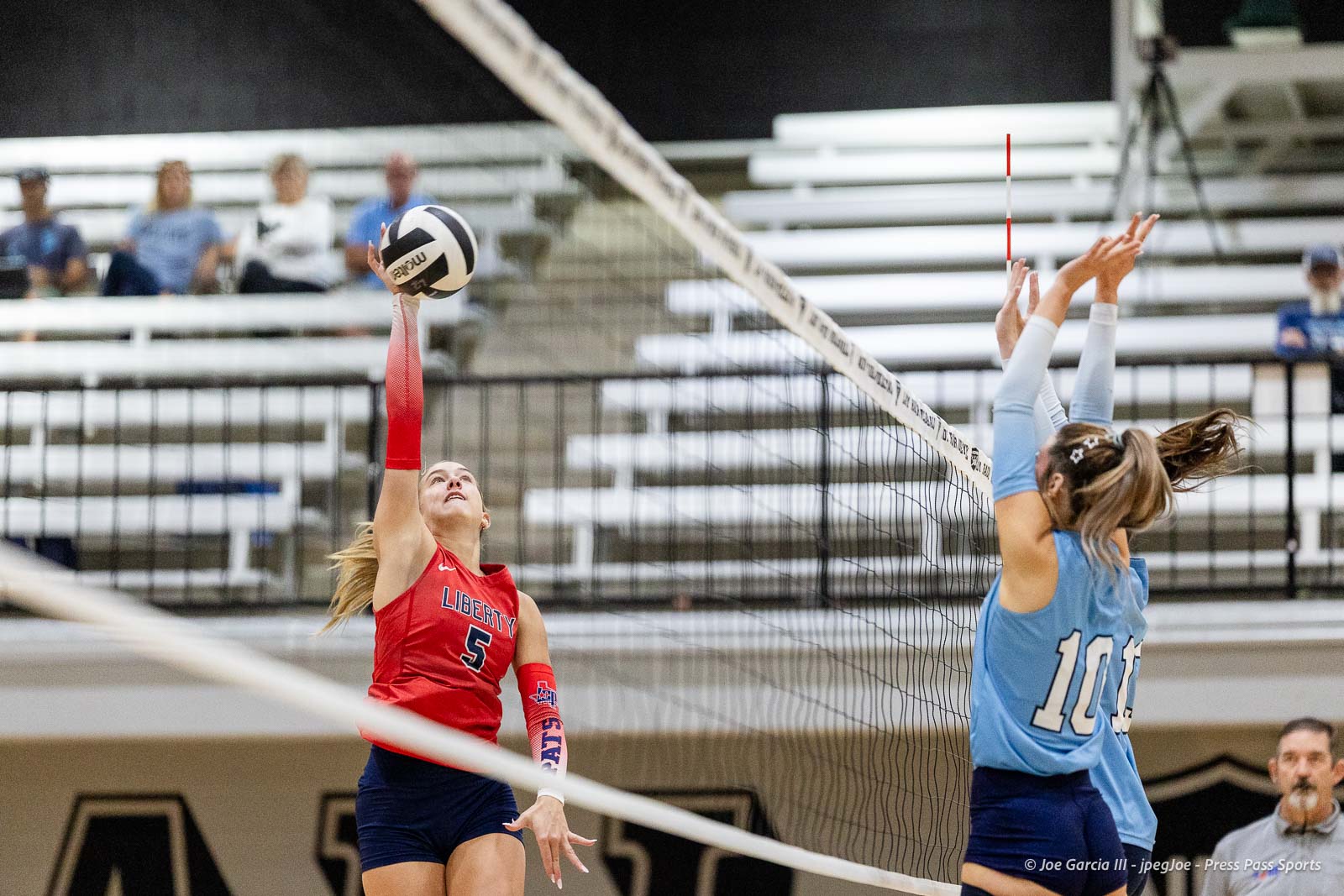 randall-showcase-2026-jpegJoe-pps-27 | Press Pass Sports Female volleyball player in a red jersey (#5) spikes the ball over the net while a blue-jersey defender jumps to block.