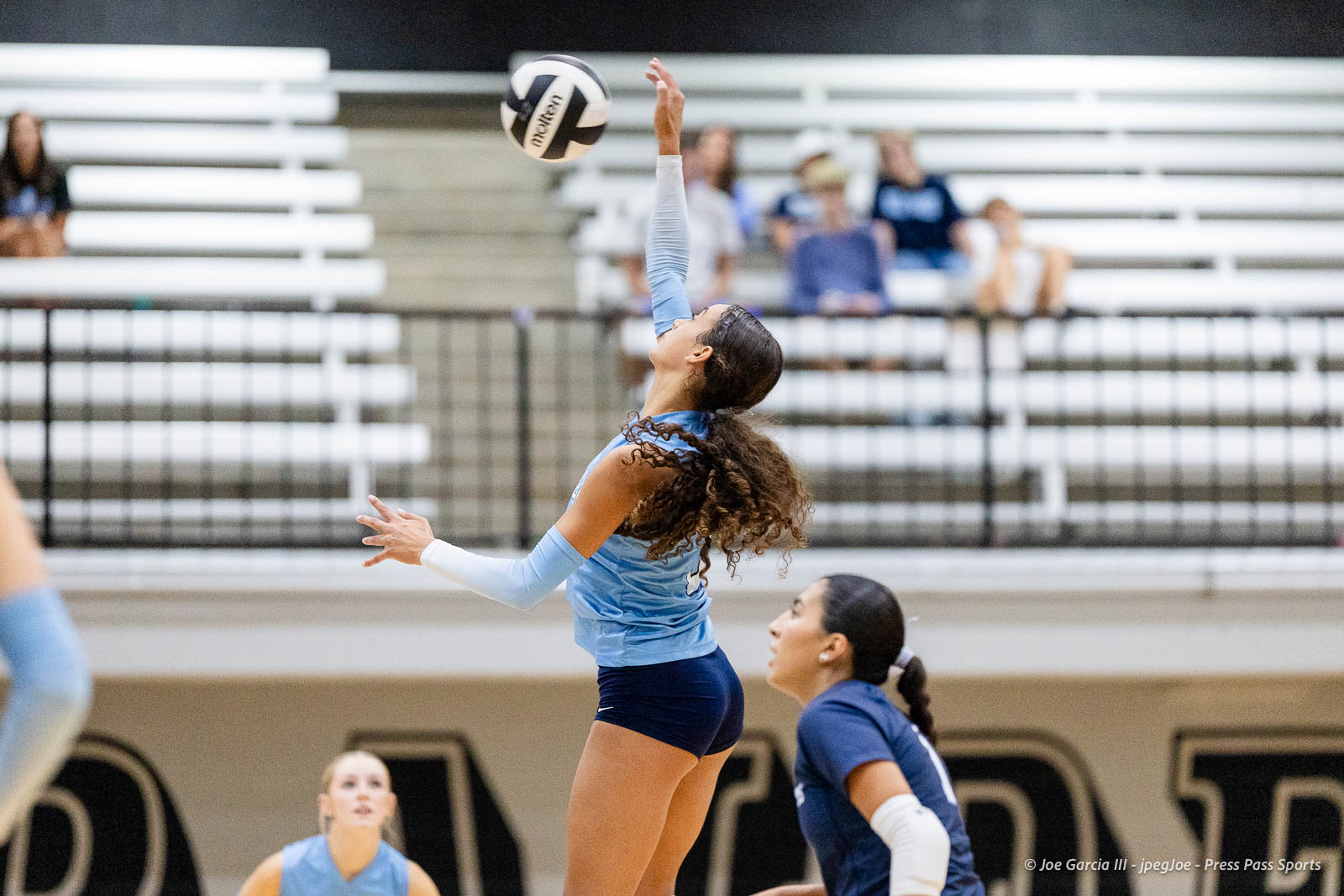 randall-showcase-2026-jpegJoe-pps-29 | Press Pass Sports Female volleyball player in a light blue uniform jumps to hit the ball during a match in a gym with bleachers in the background.