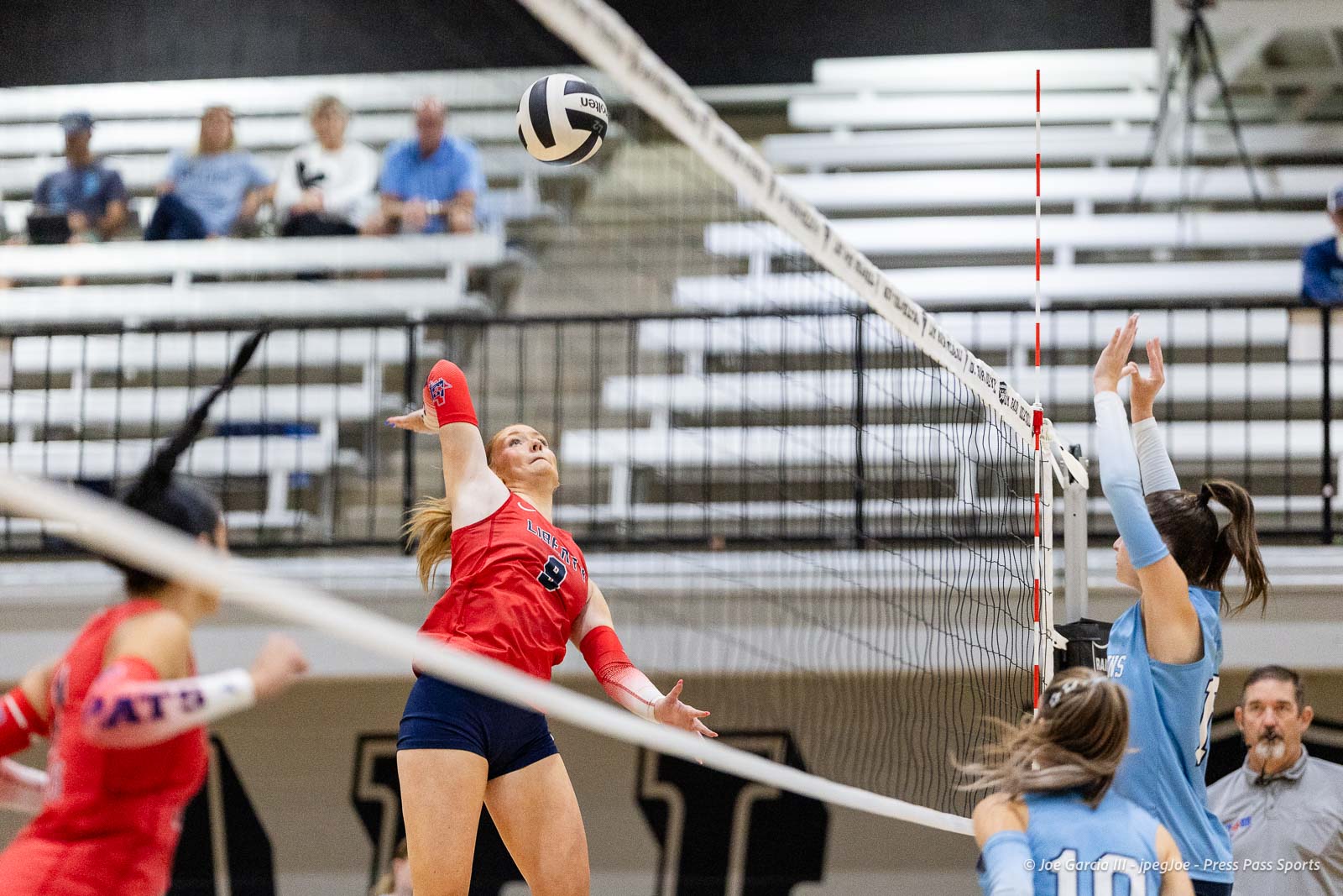 randall-showcase-2026-jpegJoe-pps-31 | Press Pass Sports Female volleyball player in red jumps to spike the ball over the net during a match in a gym.