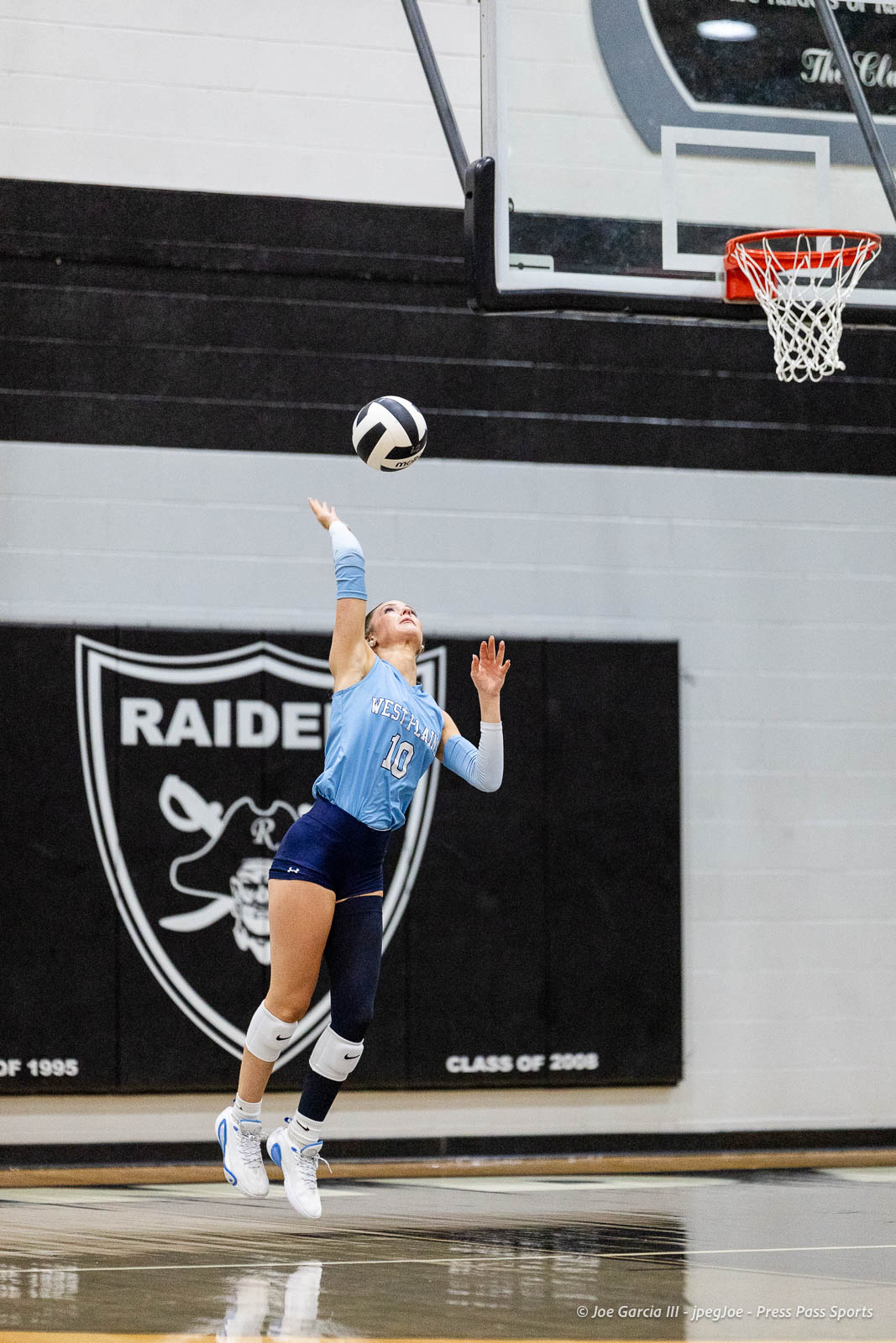 randall-showcase-2026-jpegJoe-pps-33 | Press Pass Sports Female volleyball player wearing #10 in a light blue jersey spikes a ball in a gym, Raiders banner in background.