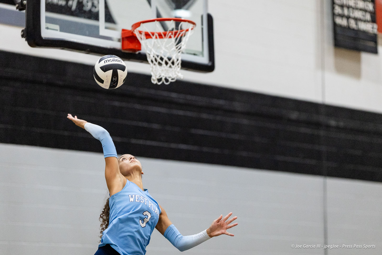 randall-showcase-2026-jpegJoe-pps-49 | Press Pass Sports Female volleyball player in a light-blue jersey reaching up to spike the ball during a game in an indoor gymnasium.
