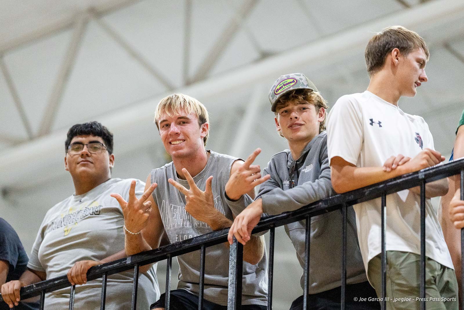 randall-showcase-2026-jpegJoe-pps-61 | Press Pass Sports Four teenage boys lean on a black railing indoors, smiling at the camera.