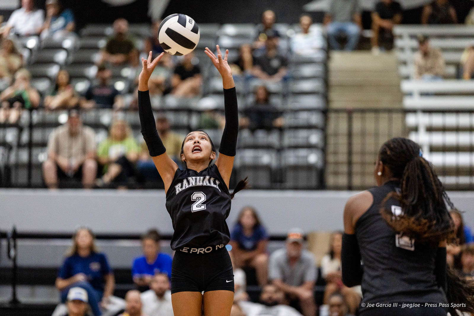 randall-showcase-2026-jpegJoe-pps-66 | Press Pass Sports Female volleyball player in a black Randall jersey #2 reaches up to set the ball, with spectators in the stands behind her.