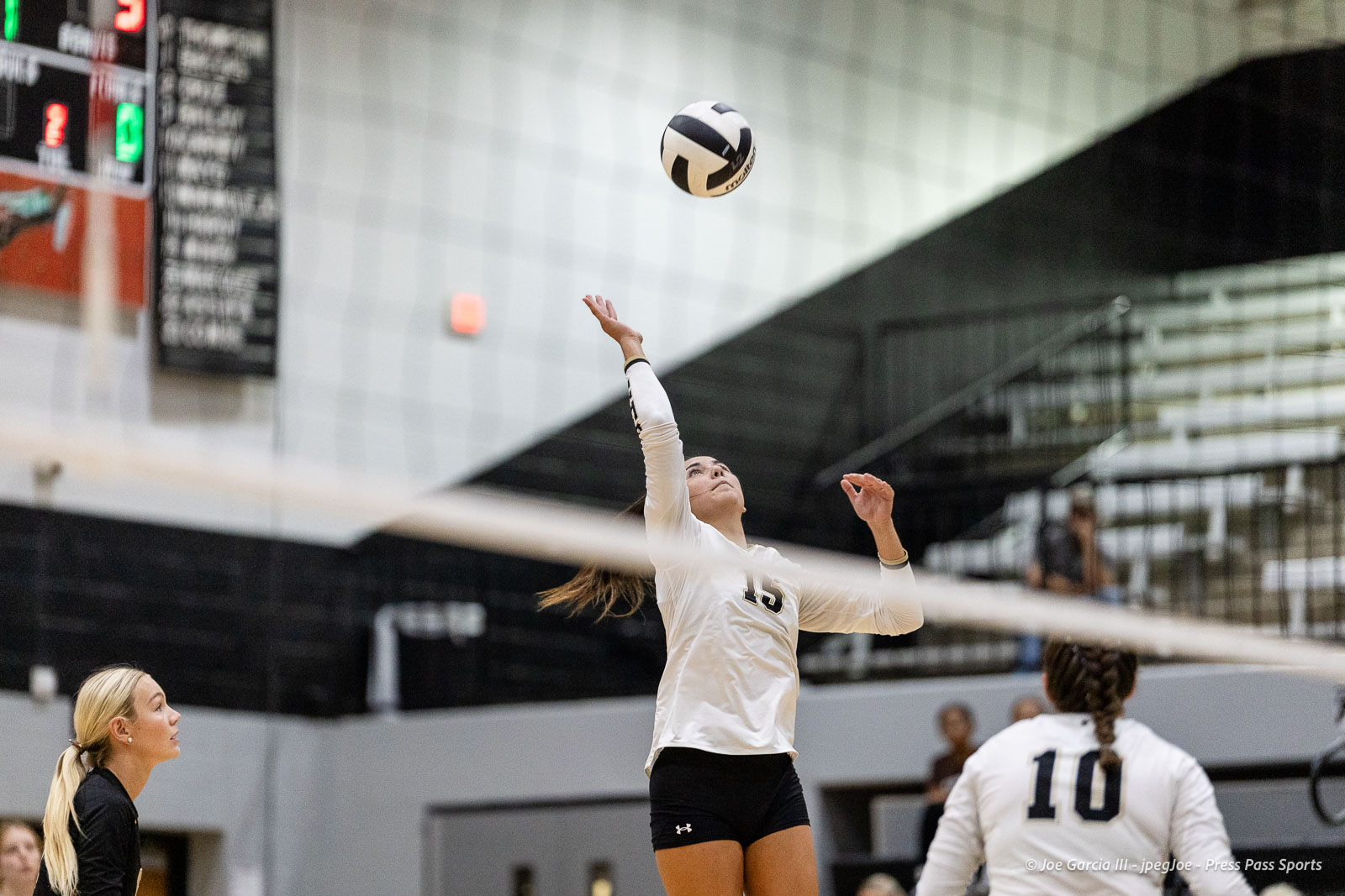 randall-showcase-2026-jpegJoe-pps-72 | Press Pass Sports Female volleyball player in a white jersey (#15) sets the ball over the net in a gym.
