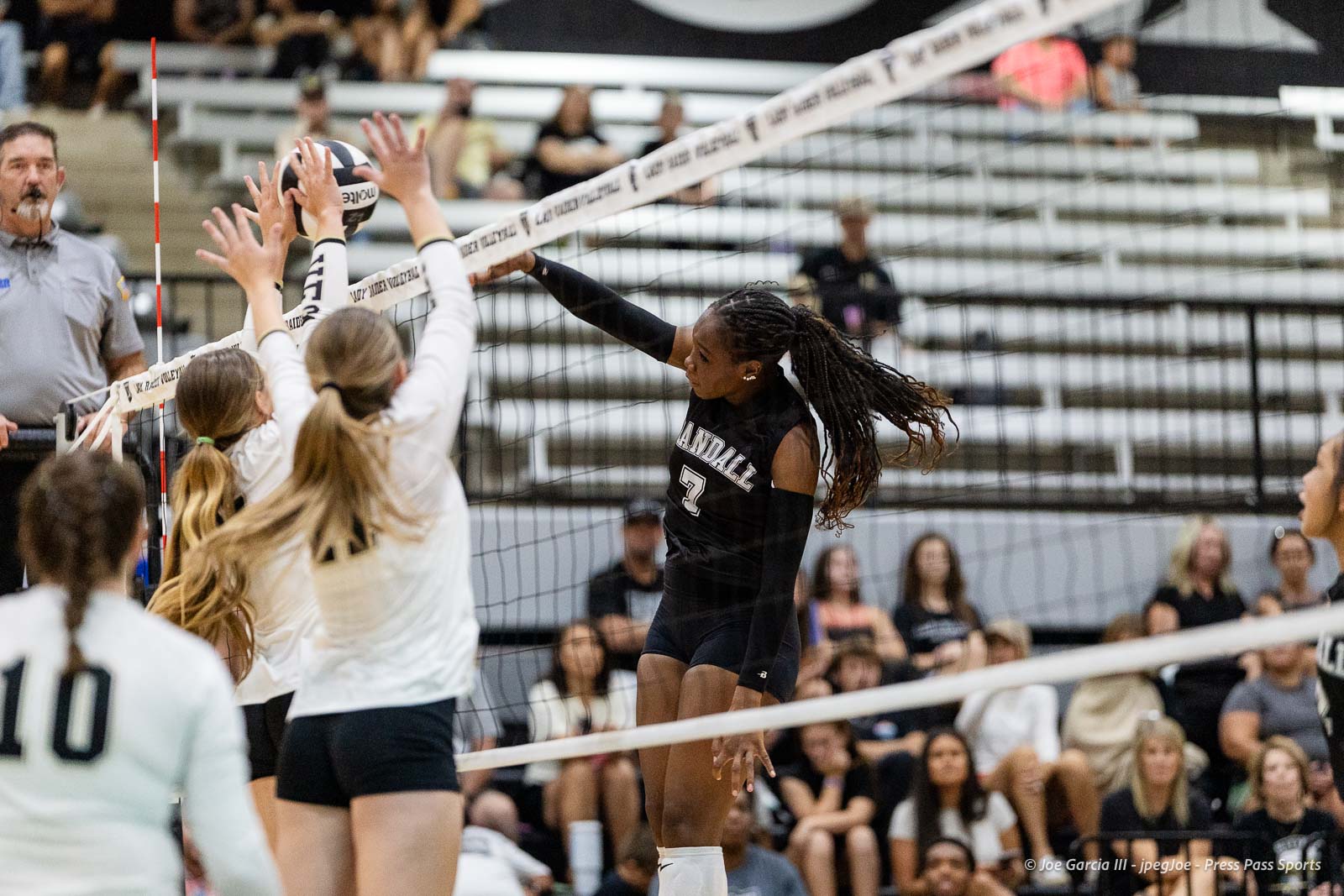 randall-showcase-2026-jpegJoe-pps-78 | Press Pass Sports Black volleyball player wearing #7 spikes the ball over the net as white-team blockers reach up in an indoor match.