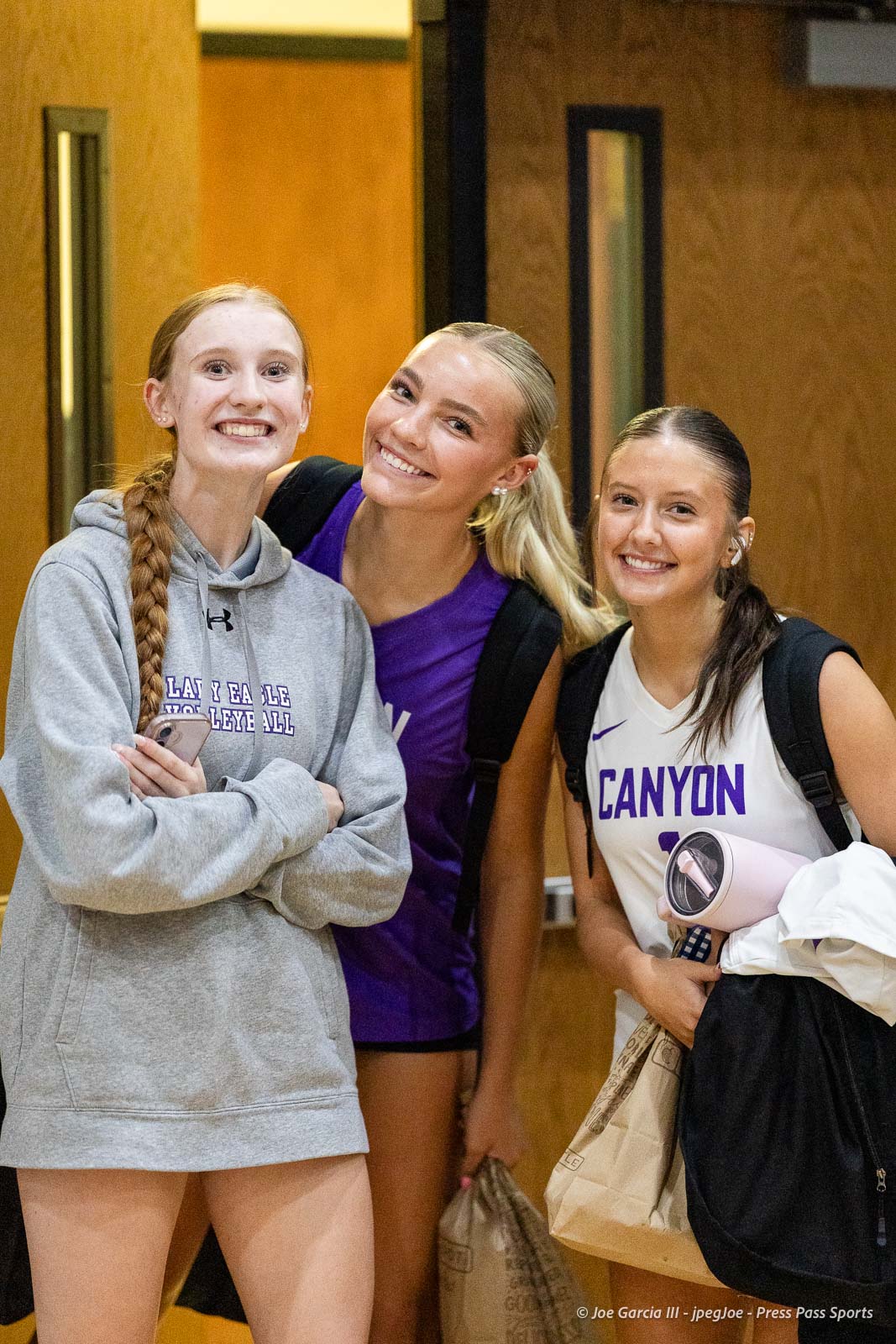 randall-showcase-2026-jpegJoe-pps-81 | Press Pass Sports Three smiling female athletes pose together in a hallway after practice, wearing volleyball Jerseys and backpacks.